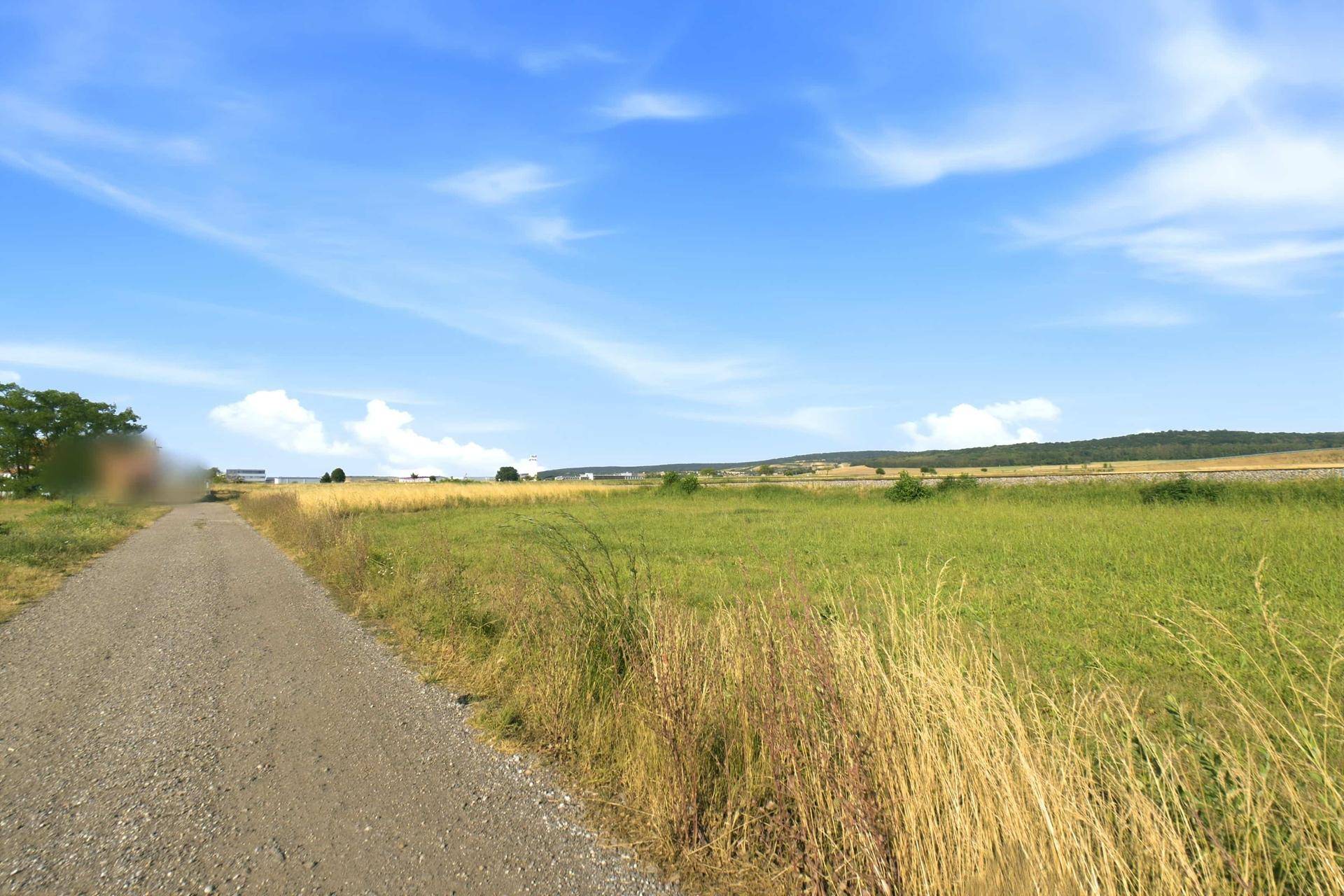 Feldweg mit grünen Wiesen und hügeliger Landschaft unter einem weiten blauen Himmel.