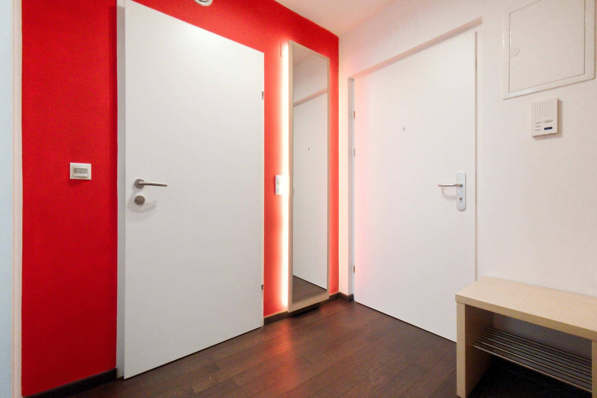 Eingangsbereich mit roter Wand, Spiegel und Sitzbank, bietet eine moderne und einladende Atmosphäre.