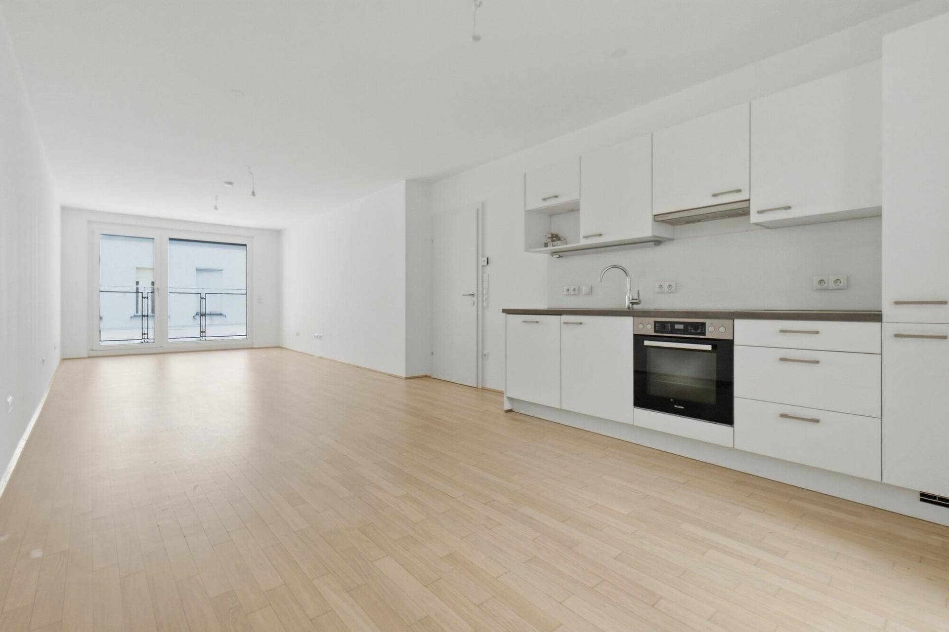 Offener Wohnbereich mit integrierter Küchenzeile und Zugang zu einem Balkon.