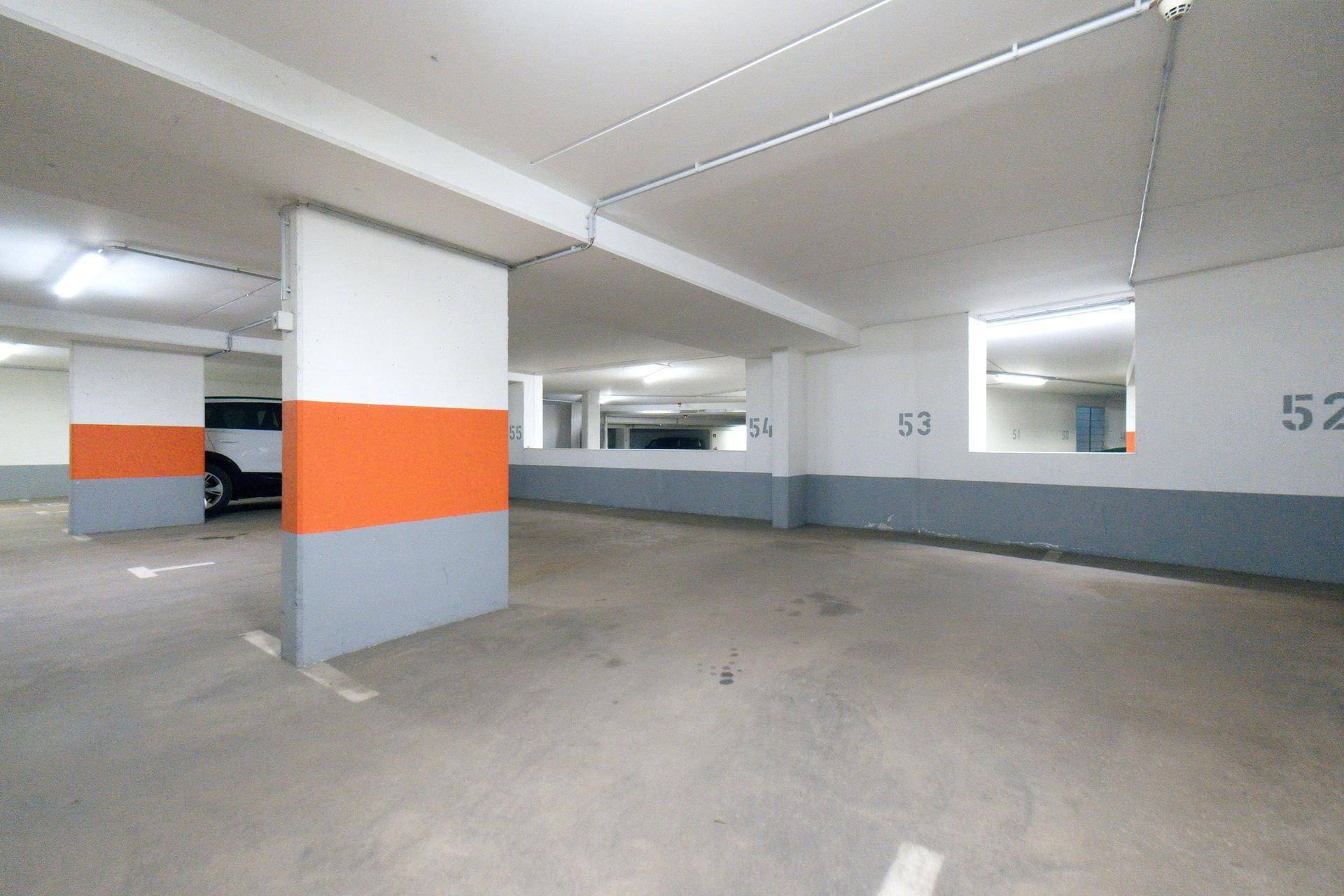 Tiefgarage mit Betonboden, orangefarbenen Säulen und reflektierenden Oberflächen.