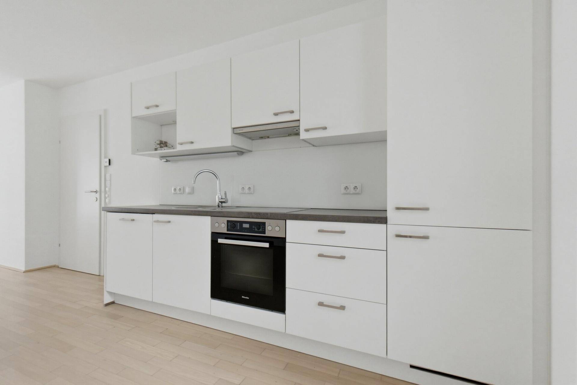 Moderne Küchenzeile mit weißen Schränken, integriertem Backofen und Spüle.