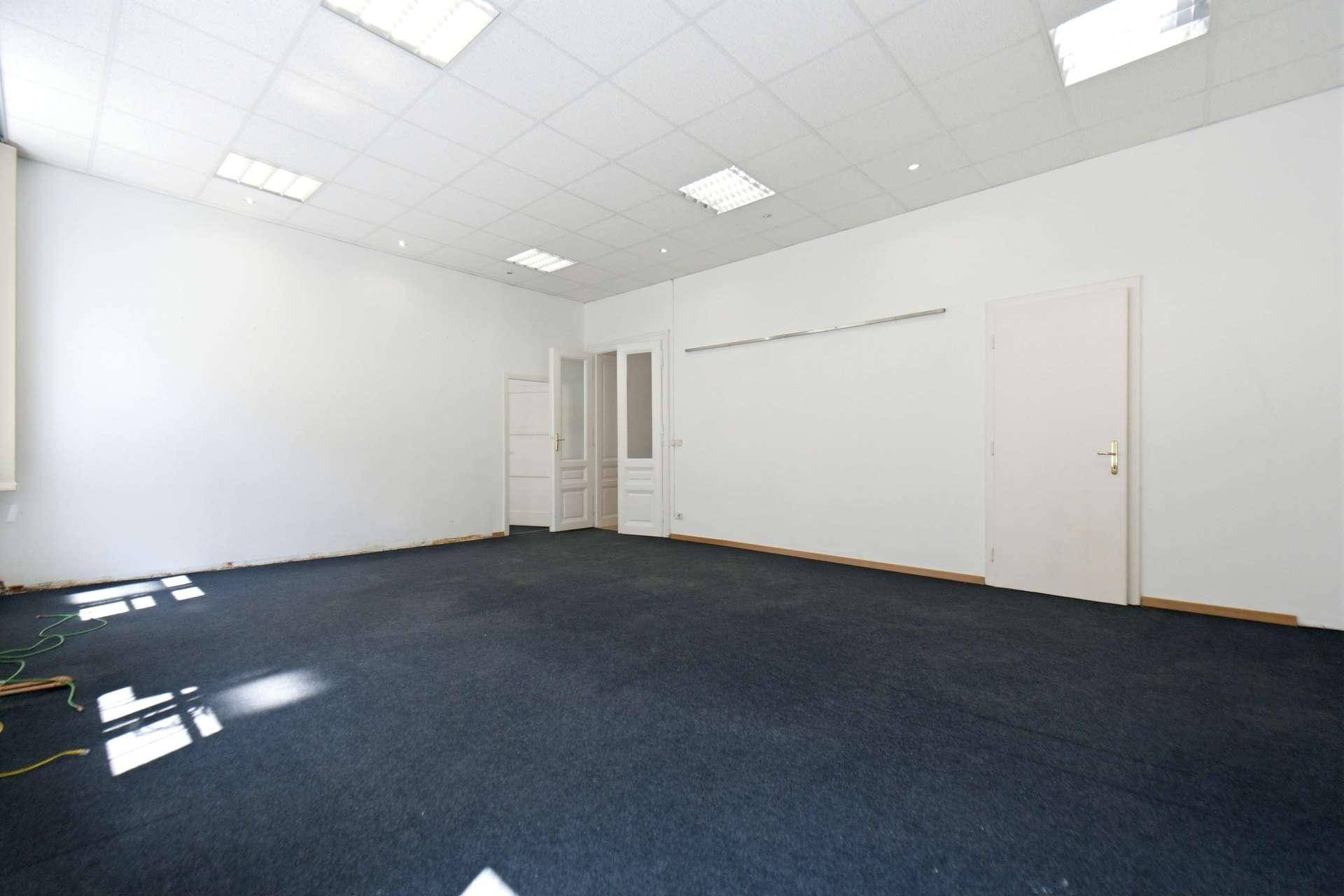 Großer, leerer Raum mit dunklem Teppichboden und mehreren weißen Türen, vielseitig nutzbar.
