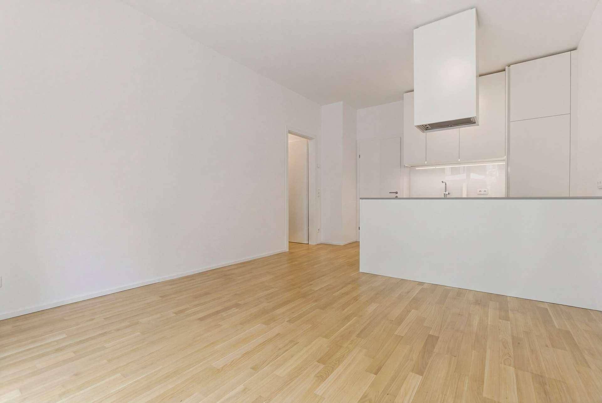 Offener Wohnbereich mit hellem Holzboden und Blick auf eine moderne, weiße Einbauküche.