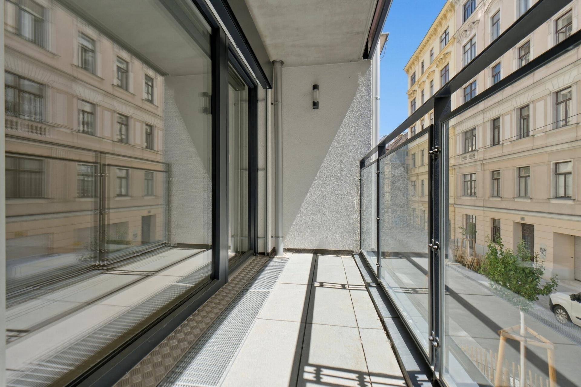 Moderner Balkon mit Glasgeländer und Blick auf die Stadtstraße und umliegende Gebäude.