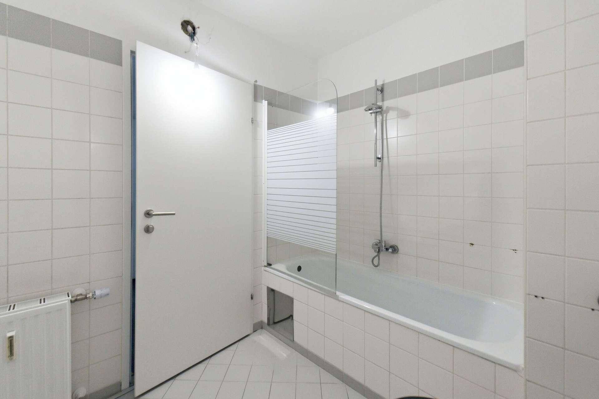 Badezimmer mit Badewanne und Duschvorrichtung, weißen Fliesen und einer modernen Tür.