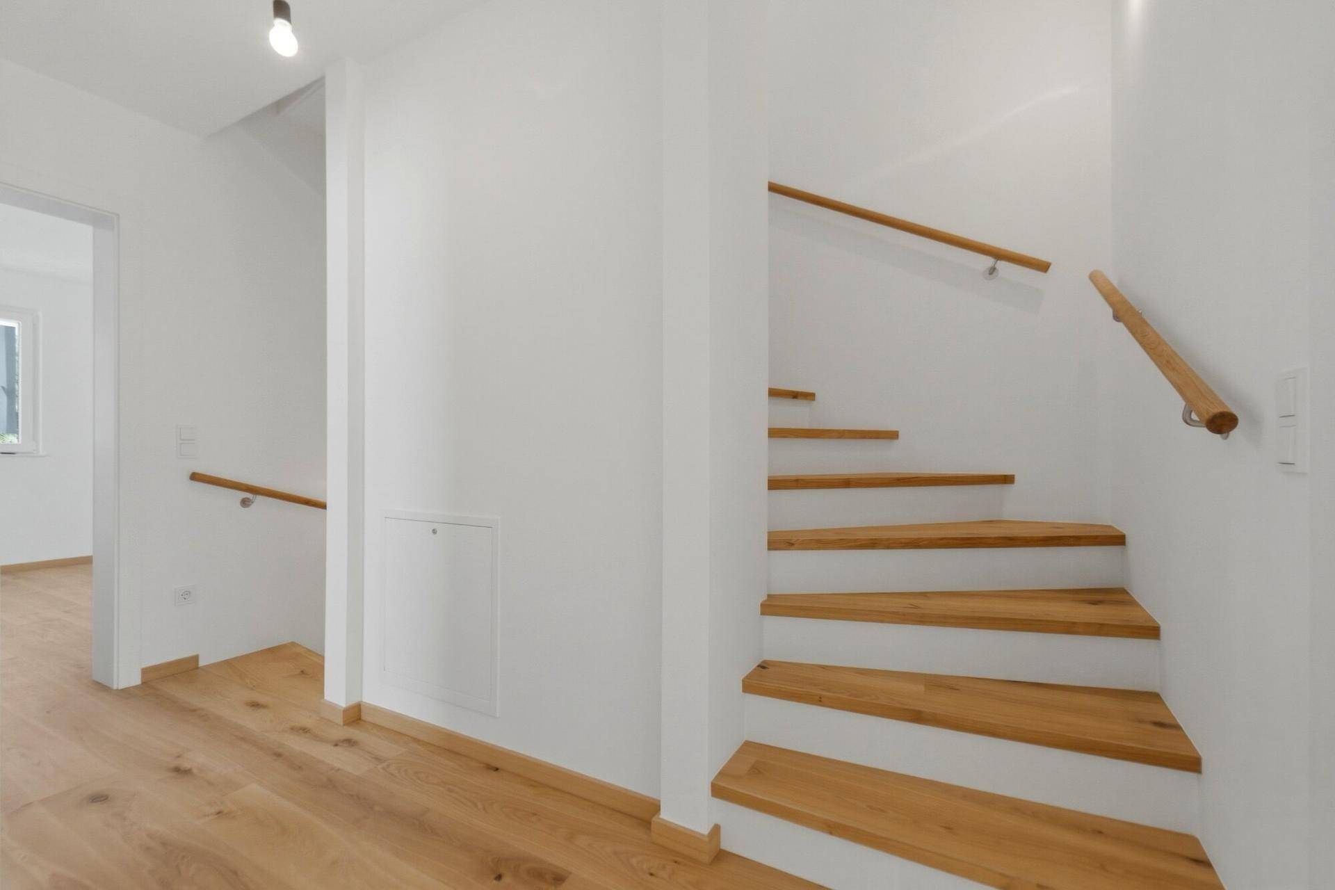 Heller Flur mit Holztreppe und passendem Handlauf, der die oberen Etagen verbindet.