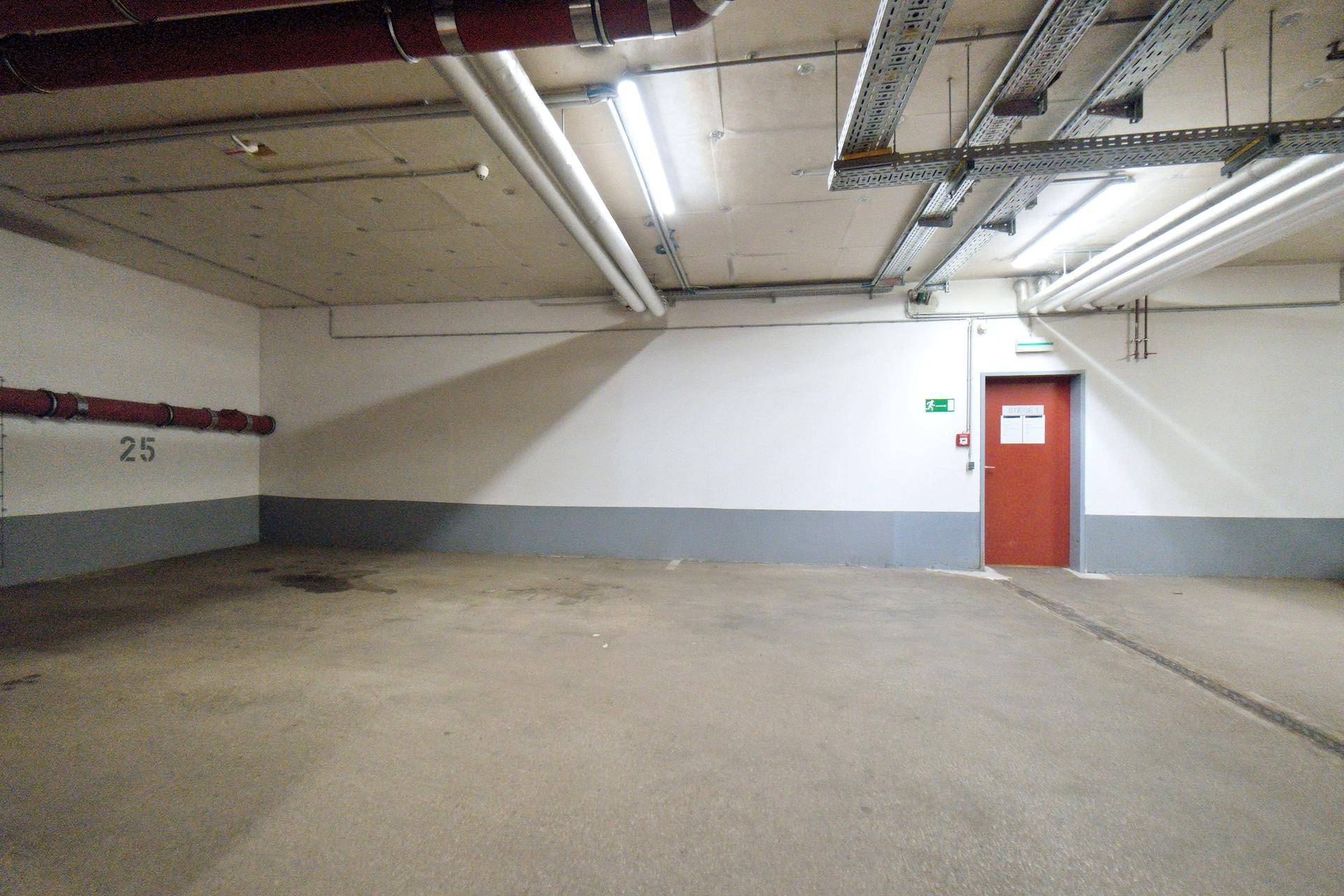 Leerer Stellplatz in der Tiefgarage mit Betonboden und roter Tür im Hintergrund.
