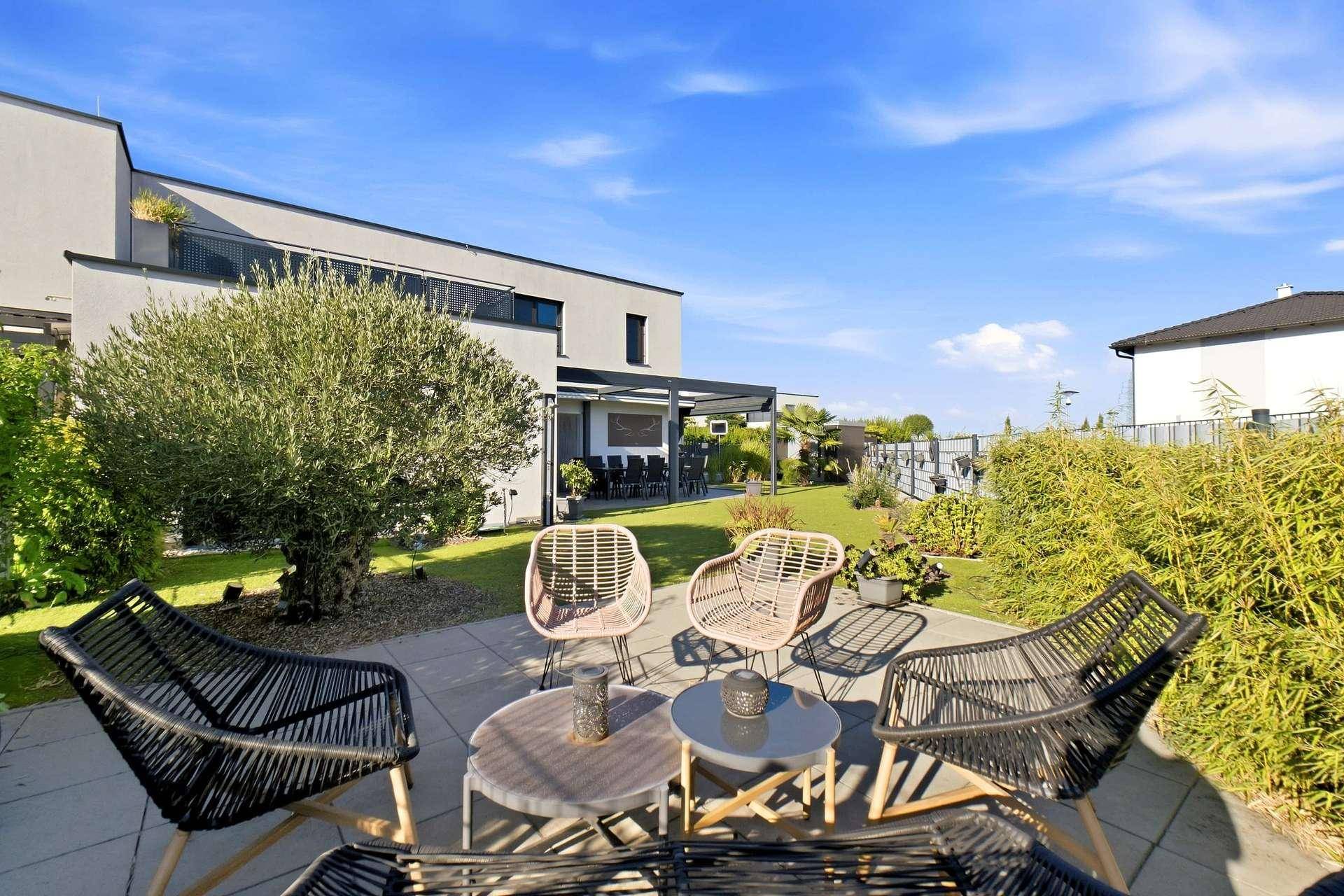Gemütlicher Sitzbereich im Garten mit modernen Korbsesseln und Blick auf die Hausfassade.