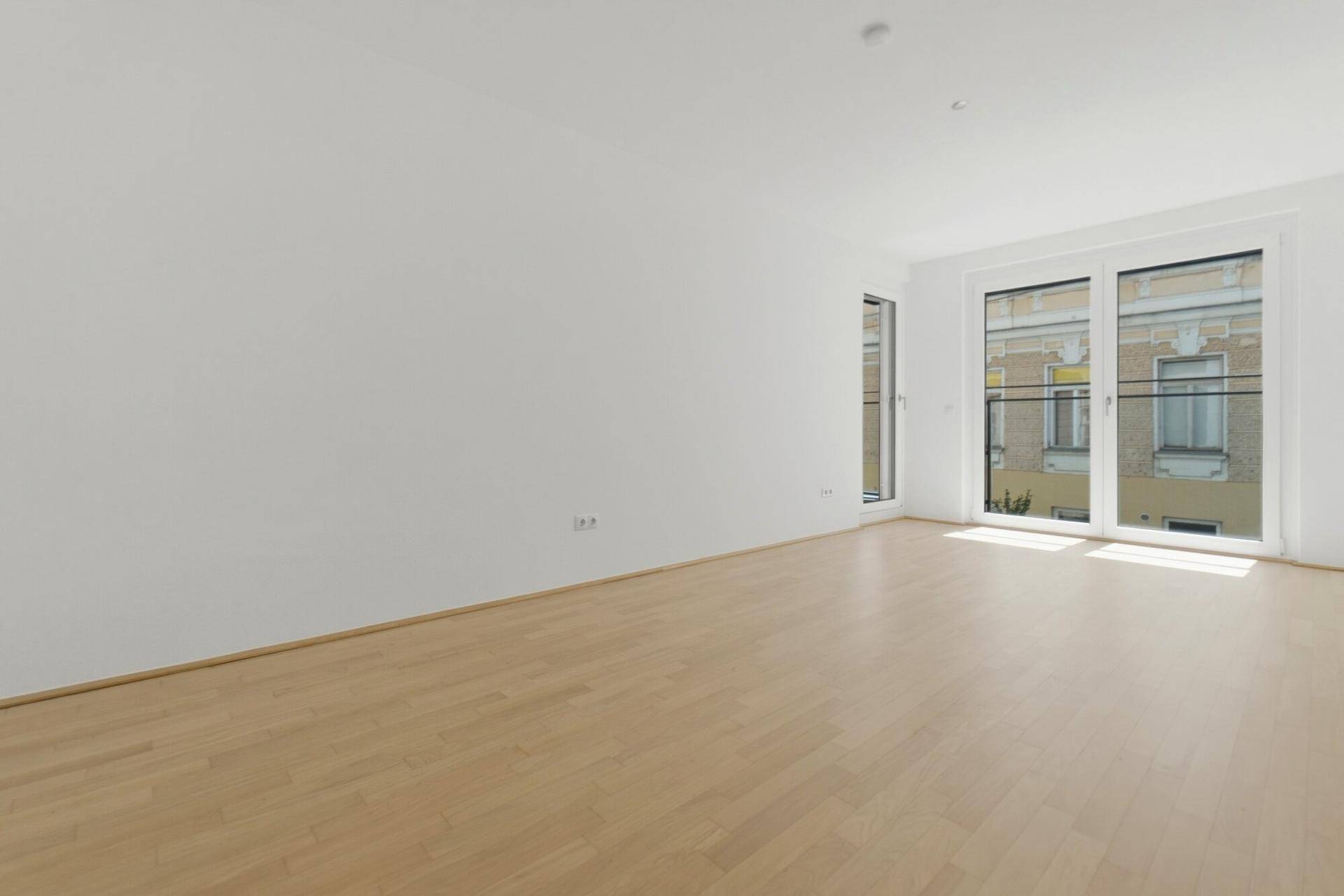 Geräumiges Wohnzimmer mit Holzboden und großen Fenstern mit Blick auf die Straße.