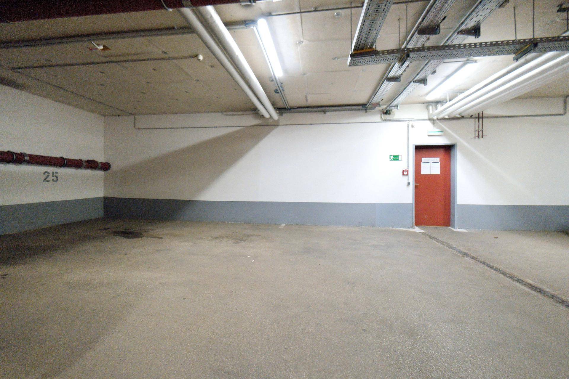 Leerer Stellplatz in der Tiefgarage mit Betonboden und roter Tür im Hintergrund.