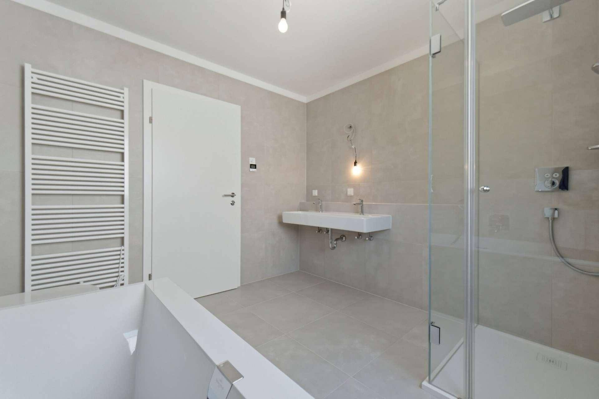 Geräumiges Badezimmer mit Doppelwaschbecken, Badewanne und begehbarer Dusche, hell gefliest.