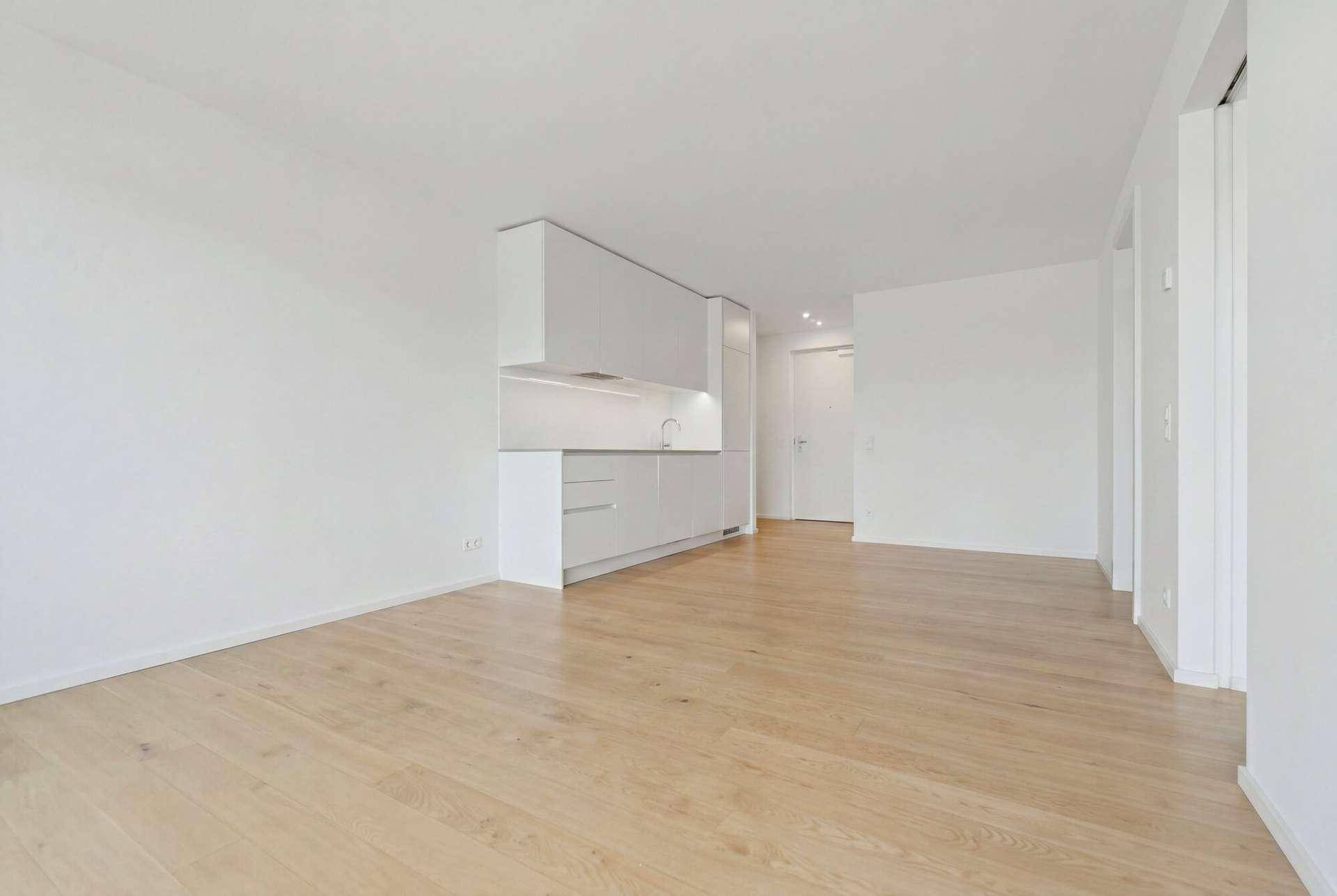 Moderne Küchenzeile mit weißen Schränken und hellem Parkettboden in offenem Raum.
