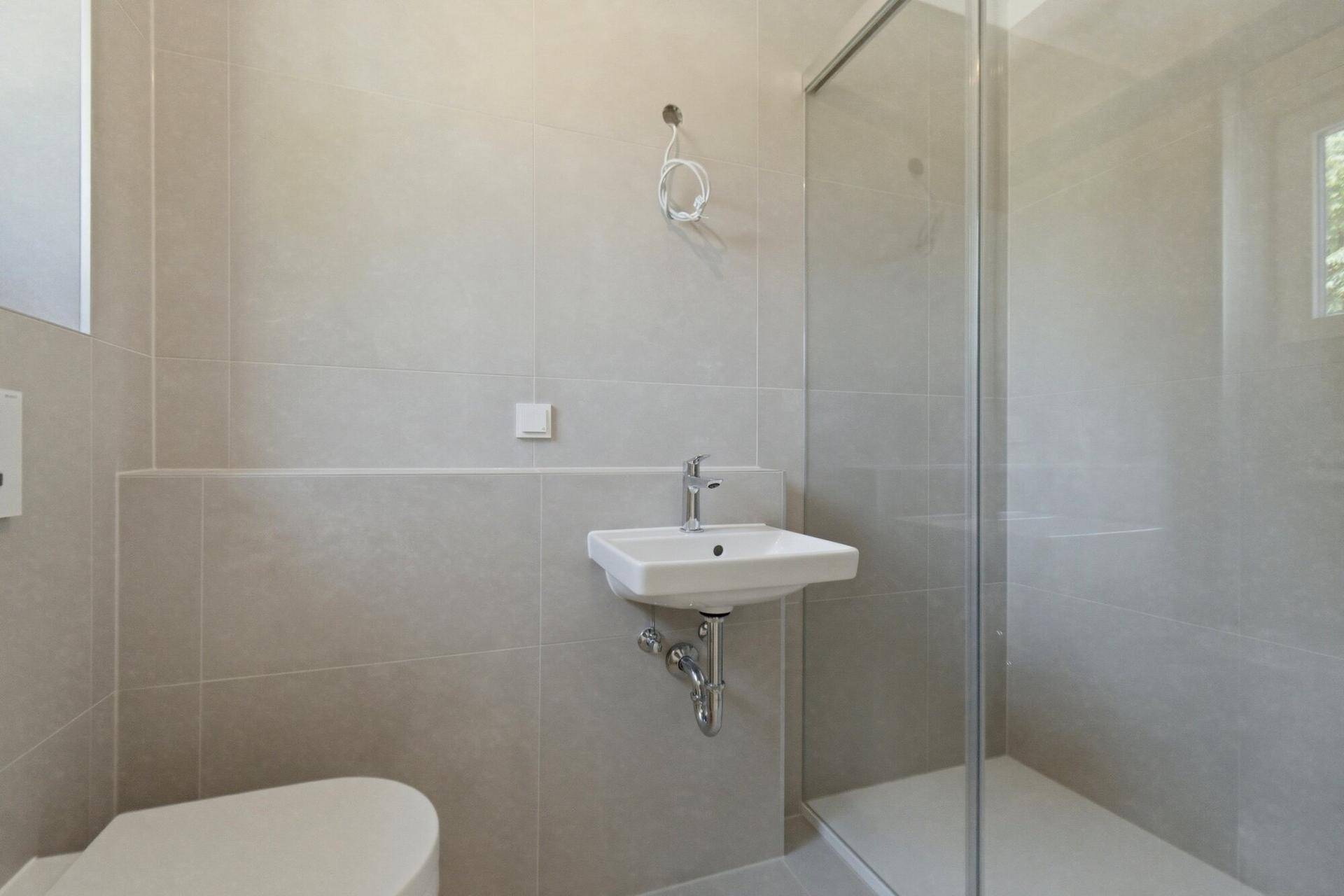 Kleines Badezimmer mit Dusche, Waschbecken, WC und Fenster für natürliche Belüftung.
