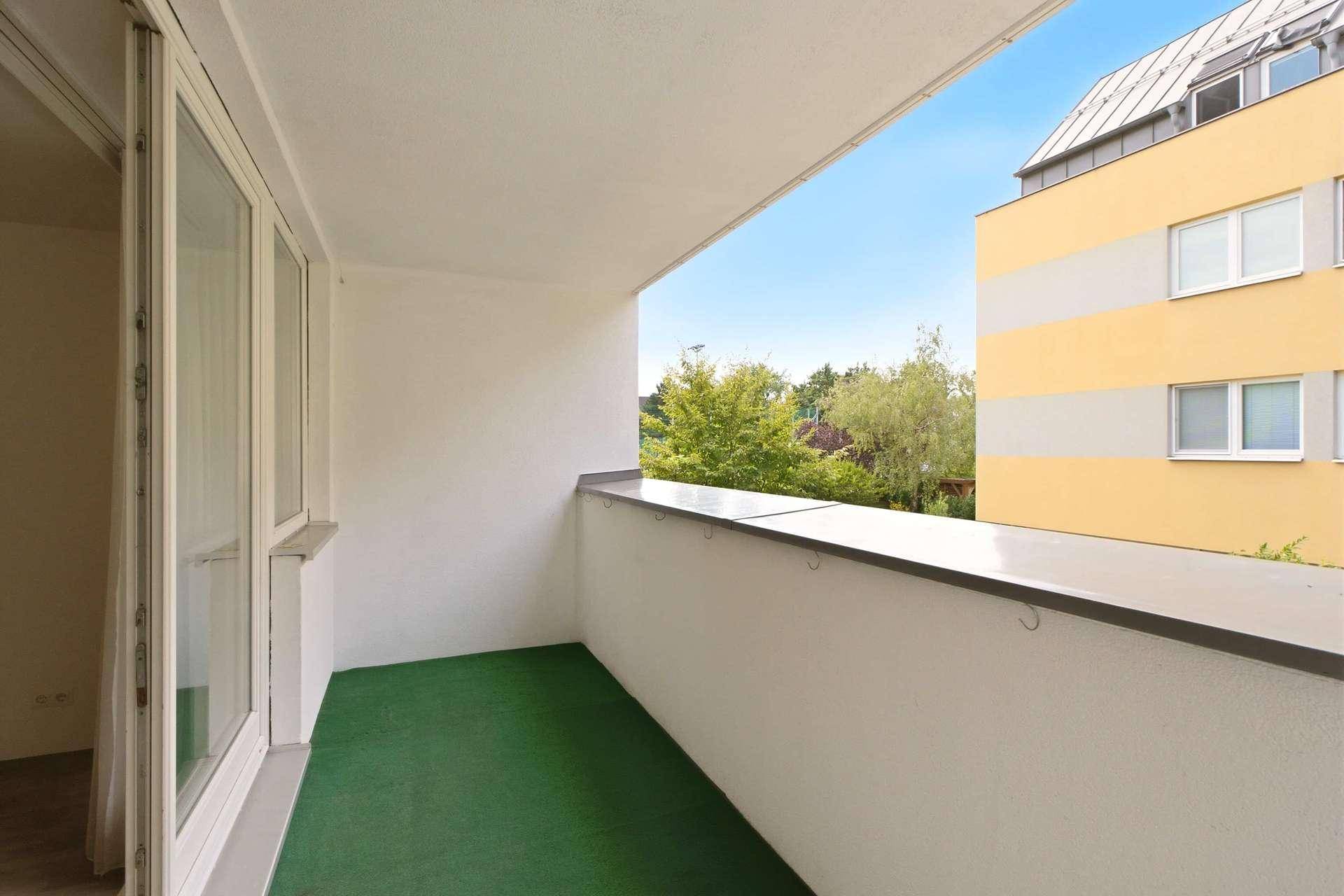 Heller Balkon mit grünem Kunstrasen und Blick auf die umliegenden Gebäude und Bäume.