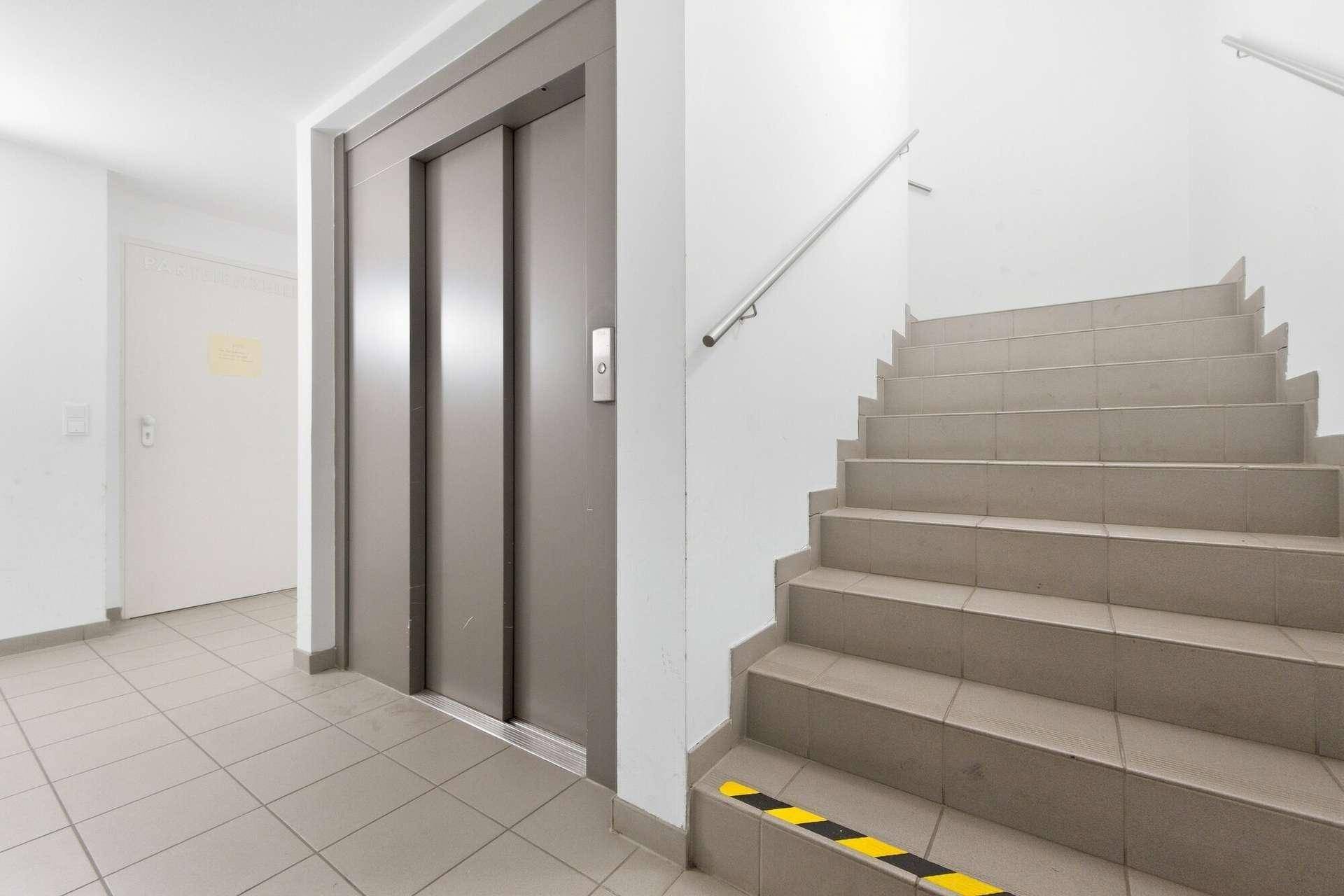 Treppenhaus mit Aufzug und Fliesenboden, das die verschiedenen Etagen verbindet.