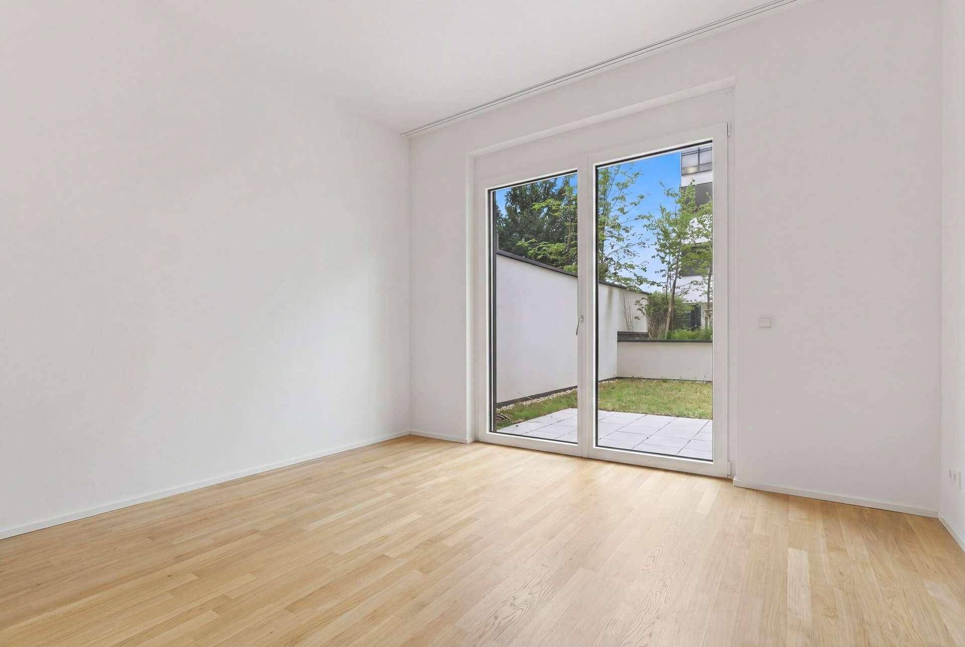 Heller Raum mit Holzboden und großen Schiebetüren, die zu einem kleinen Gartenbereich führen.