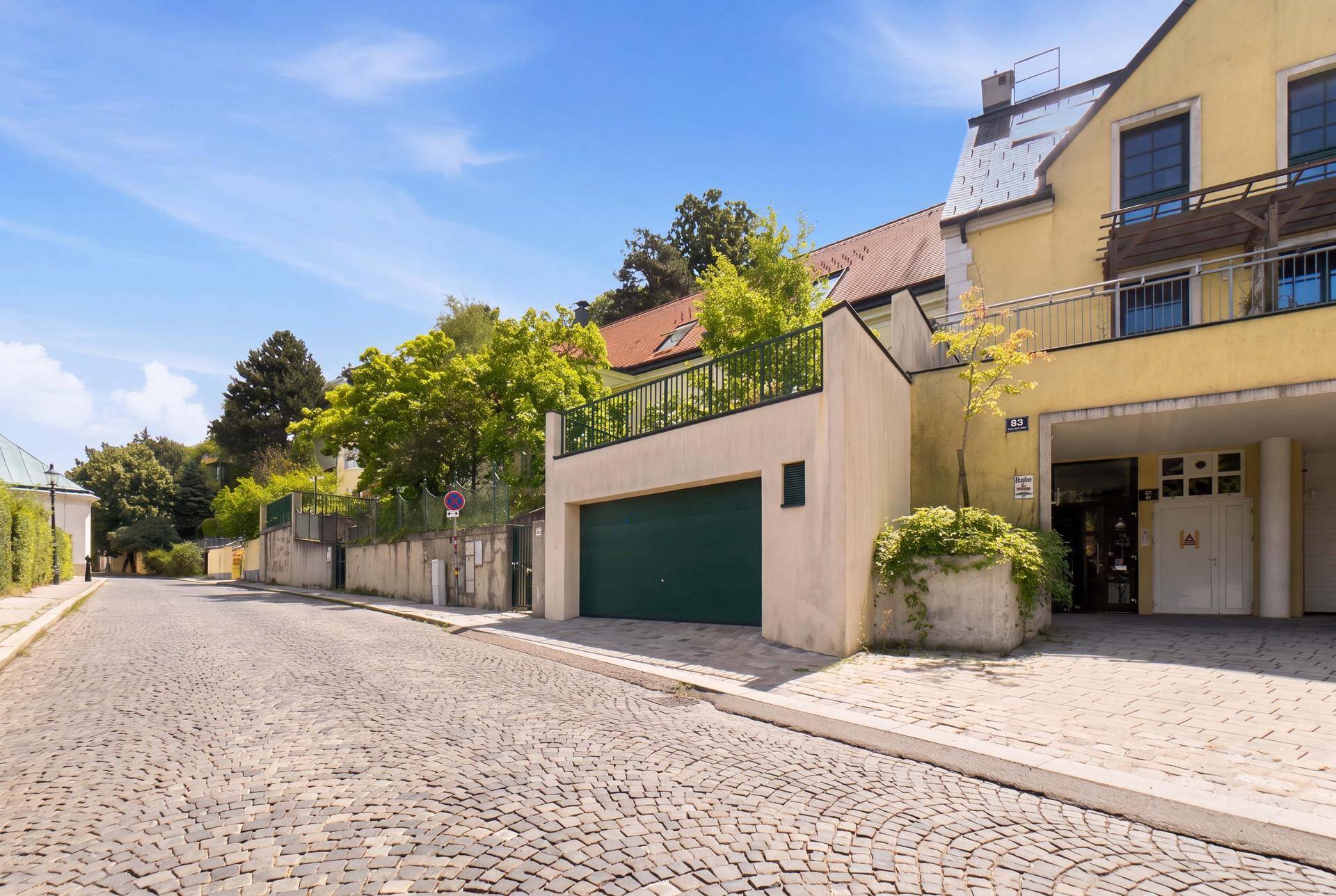 Außenansicht eines Wohnhauses mit gepflasterter Straße und Garagenzufahrt unter blauem Himmel.