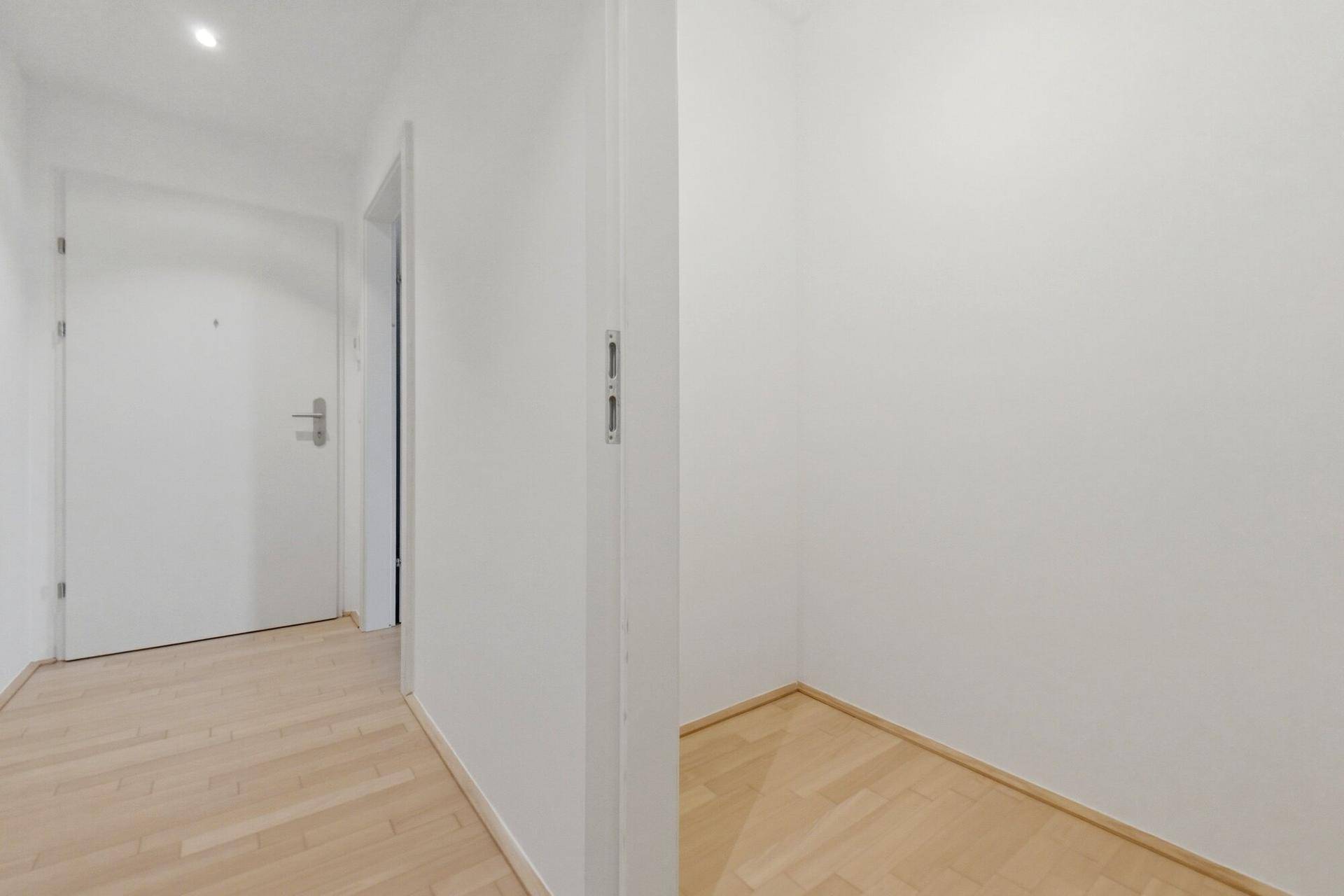 Flur mit Holzboden, der zu einem kleinen, leeren Abstellraum führt.