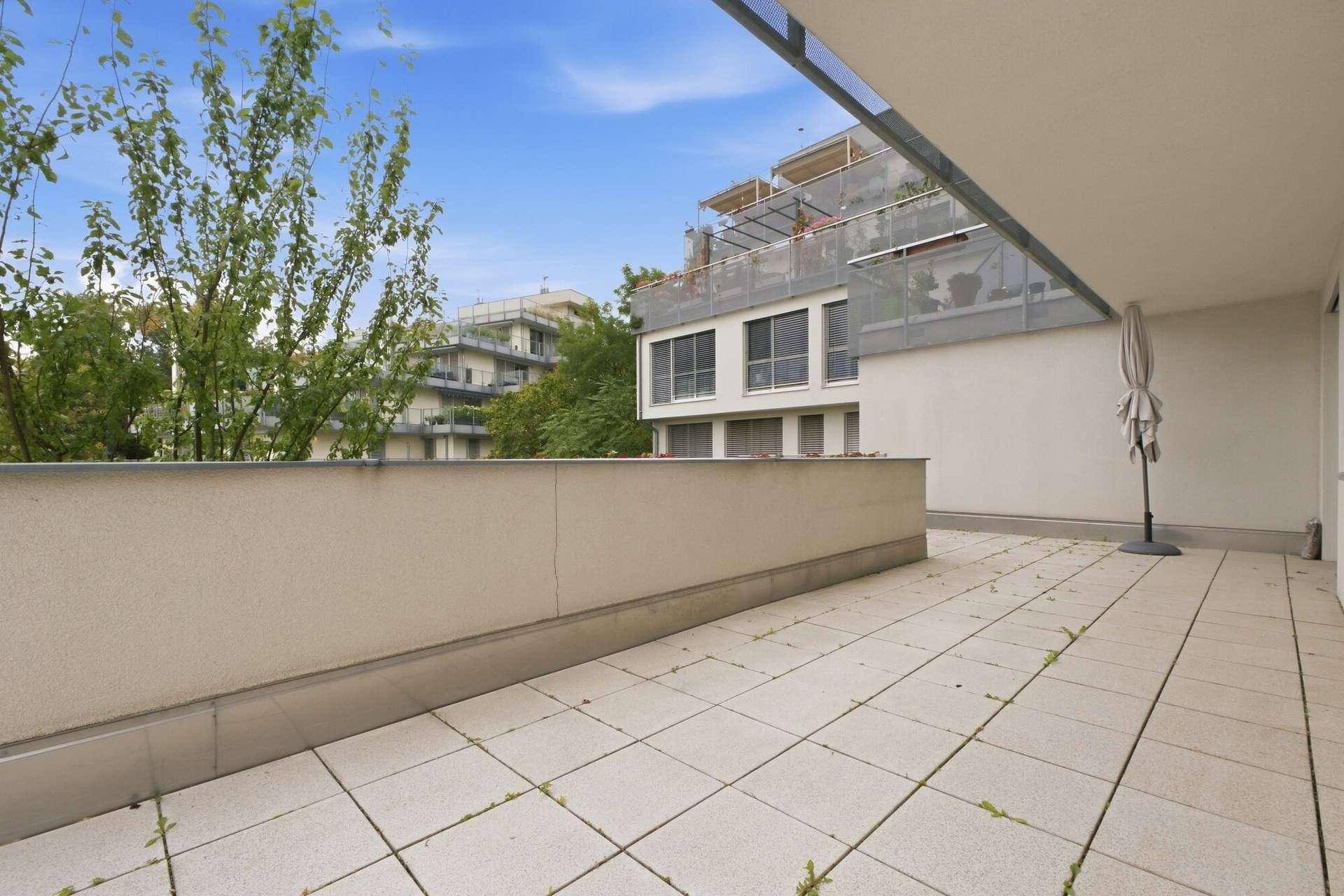 Weitläufige Außenterrasse mit Fliesenboden und Blick auf die umliegenden Gebäude und Grünflächen.