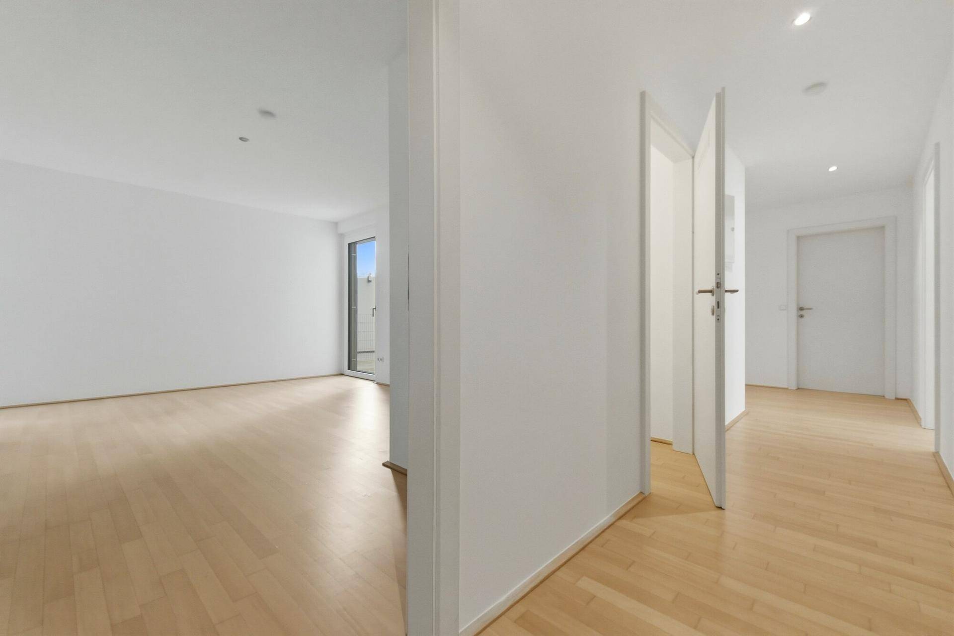Heller Flur mit Holzboden und Blick in ein angrenzendes, leeres Zimmer.