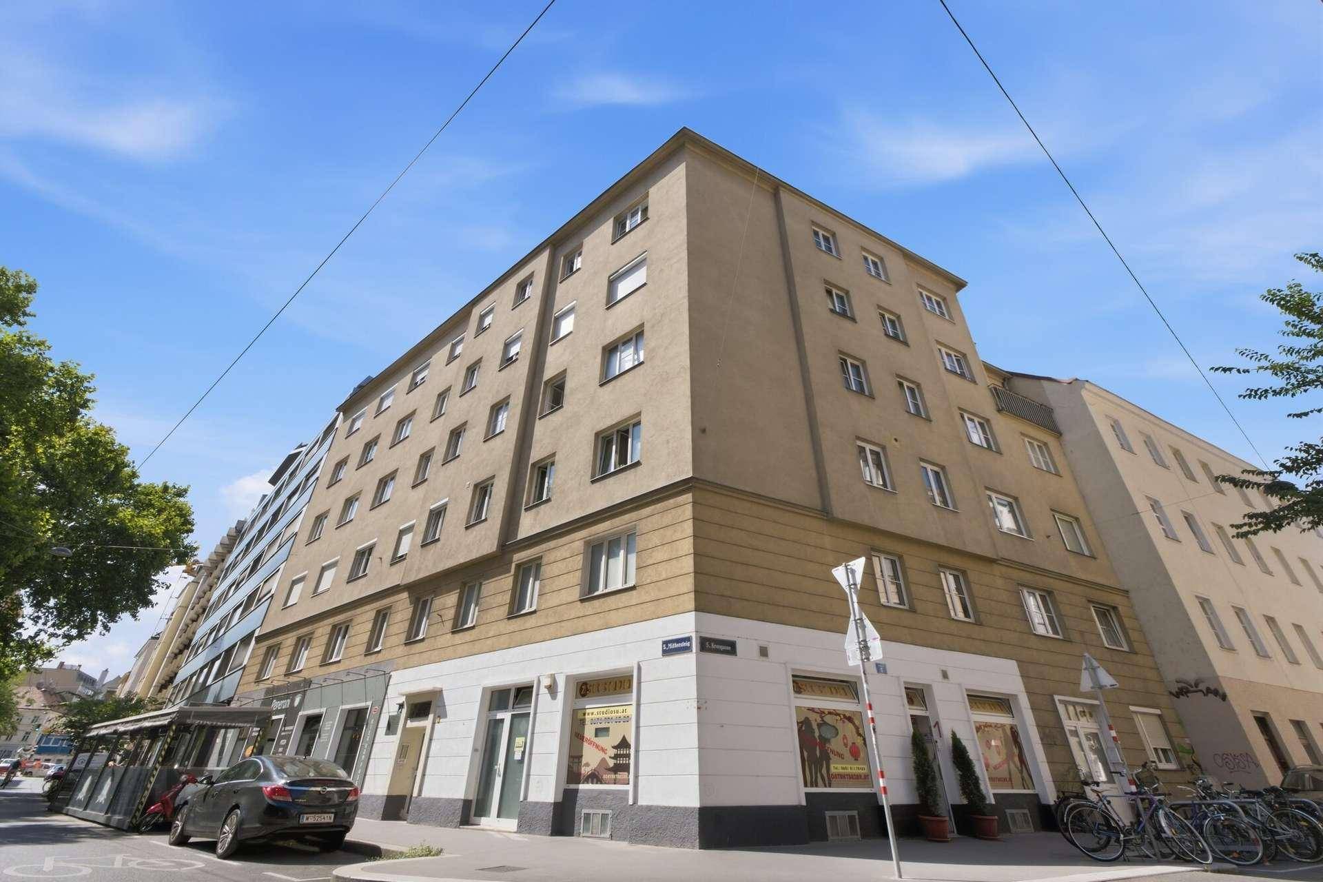 Eckgebäude mit mehreren Etagen, Geschäften im Erdgeschoss und urbaner Umgebung.