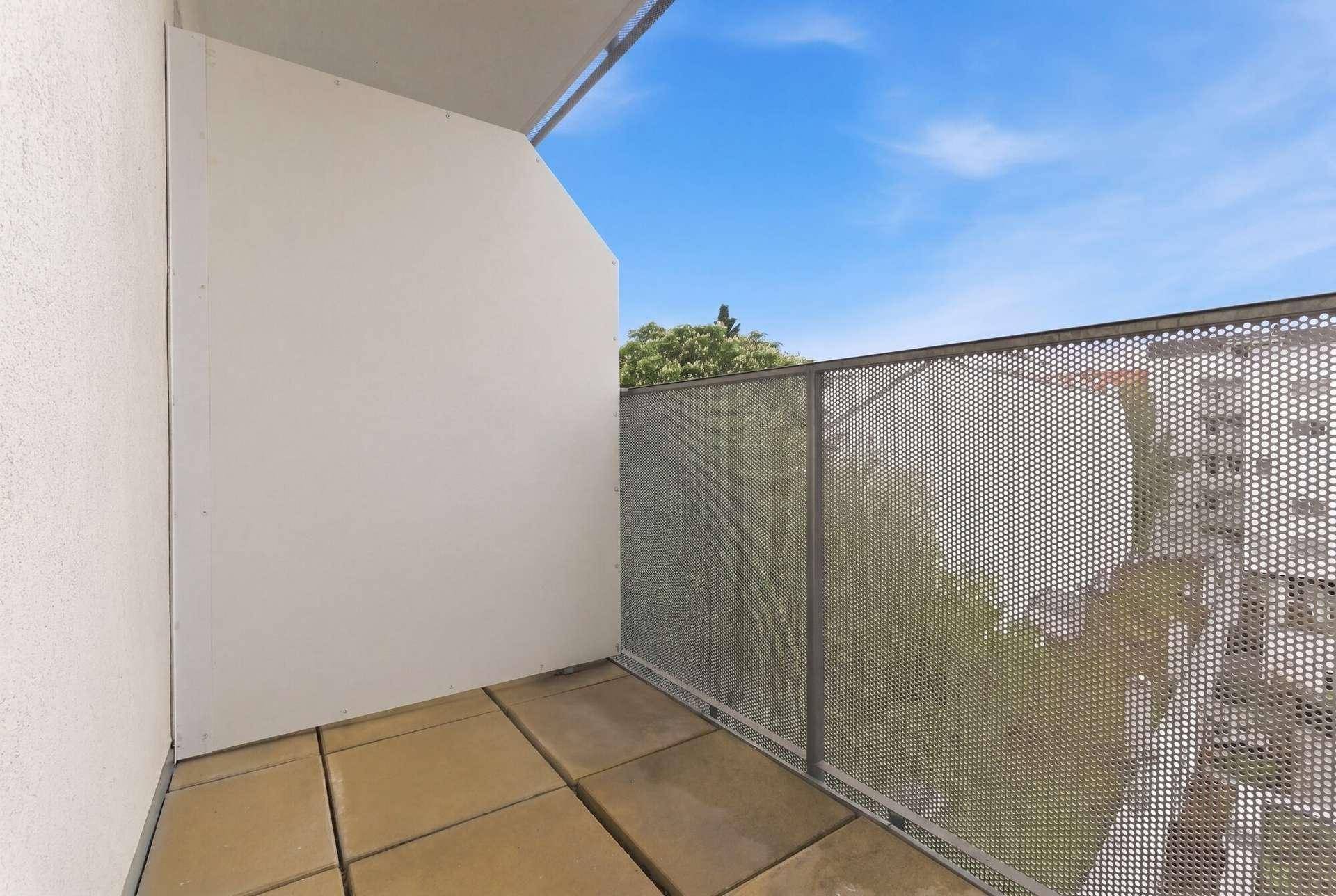Kleiner Balkon mit Fliesenboden und perforiertem Metallgeländer unter blauem Himmel.