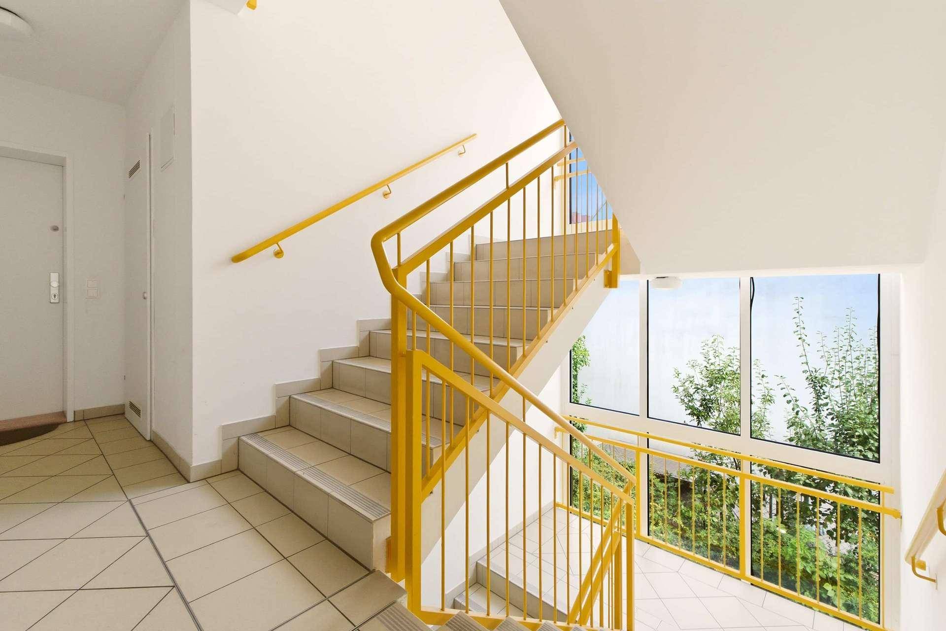 Helles Treppenhaus mit gelben Geländern und großen Fenstern für viel Tageslicht.