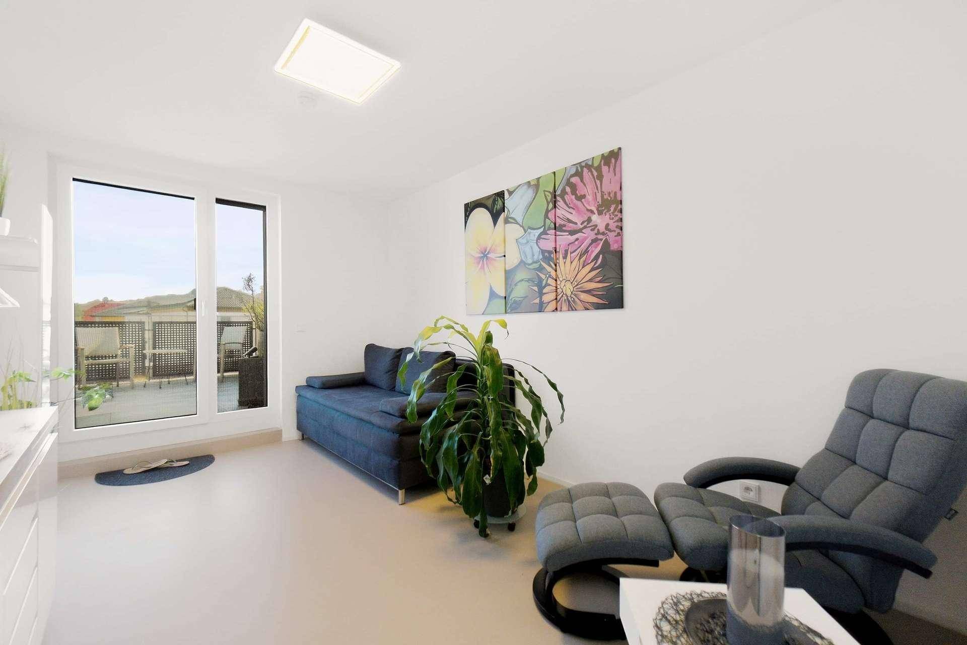 Helles Wohnzimmer mit modernem Sofa, Sessel und Zugang zur Terrasse.