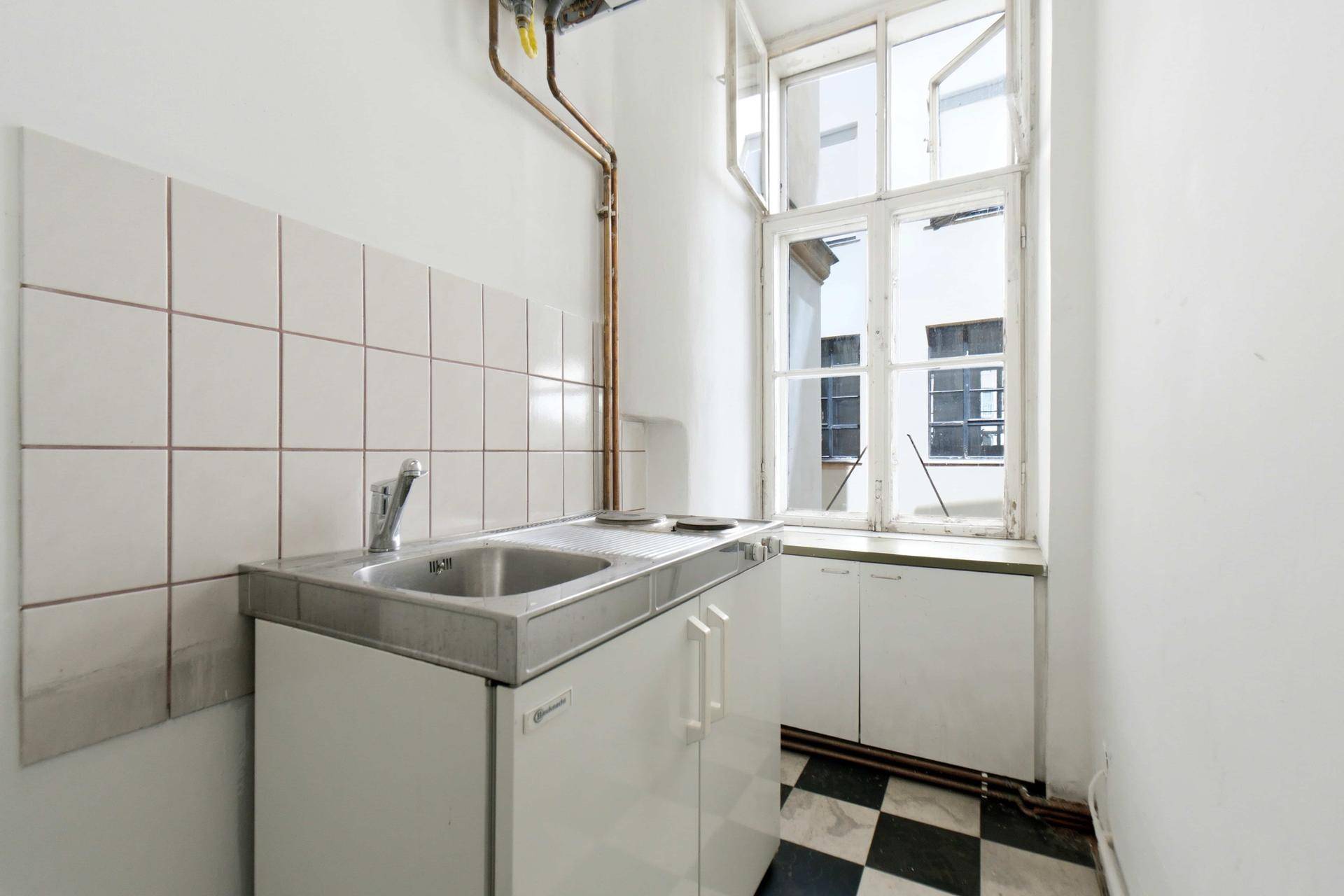 Kleine Küche mit Spüle, Unterschränken und Fenster zum Innenhof.