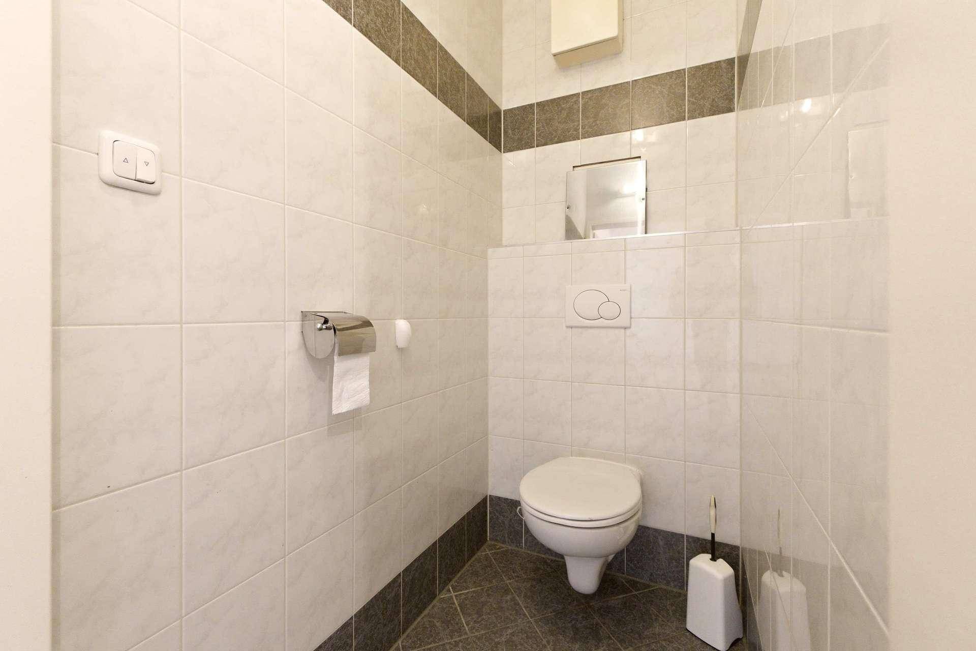 Modern gefliestes Gäste-WC mit wandhängender Toilette und dunklem Boden.