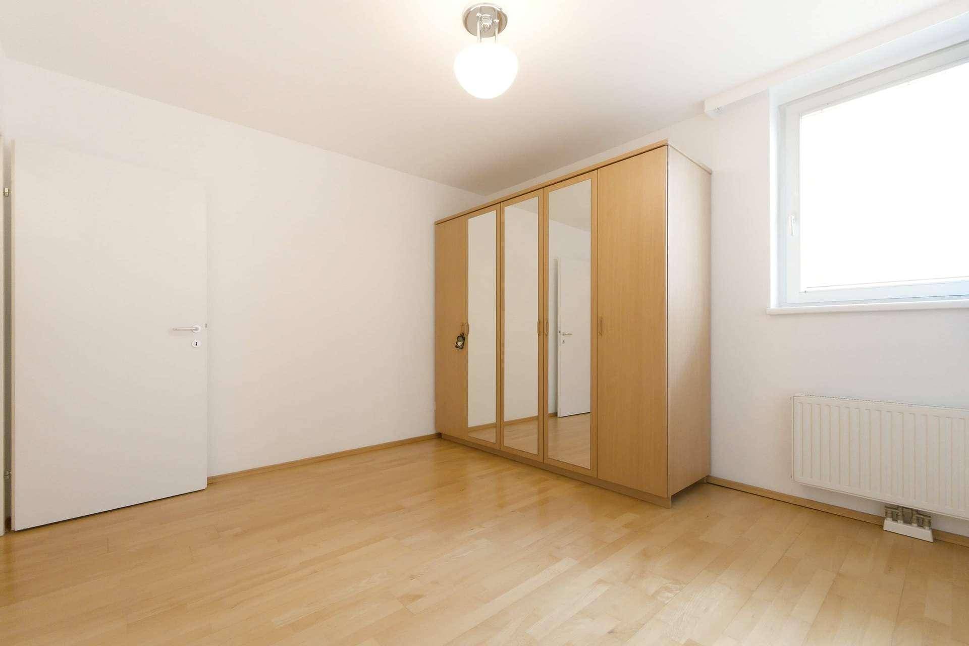 Geräumiges Schlafzimmer mit Parkettboden, Kleiderschrank und Fenster für natürliches Licht.