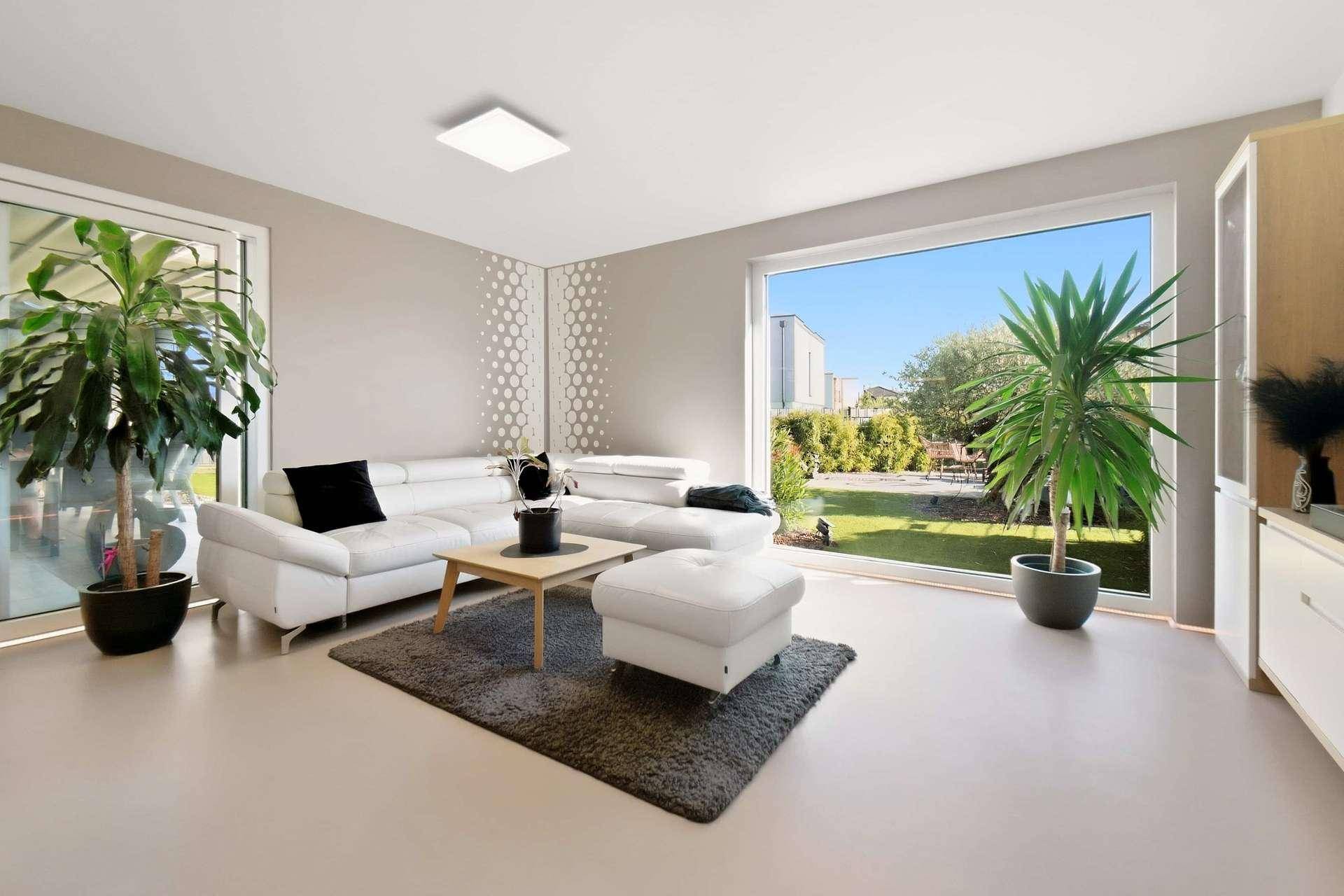 Helles Wohnzimmer mit weißem Sofa, modernem Teppich und großem Fenster zum Garten.