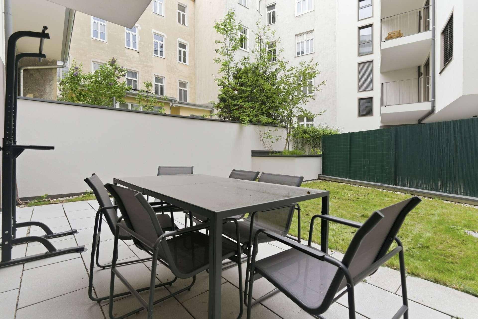 Gemütliche Terrasse mit Esstisch und Stühlen, umgeben von Grünflächen und Gebäuden.