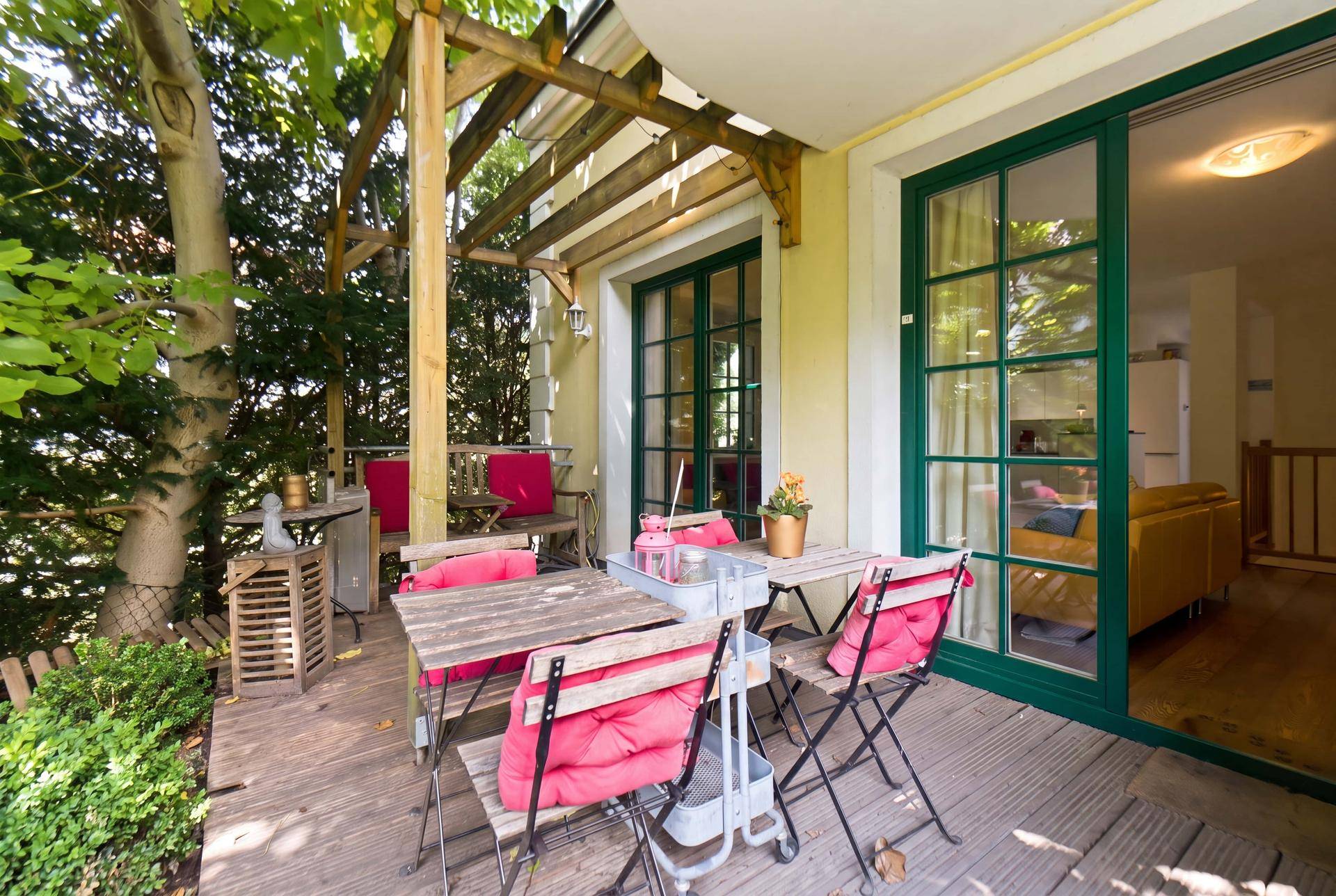 Gemütliche Holzterrasse mit Esstisch und roten Kissen, umgeben von viel Grün.