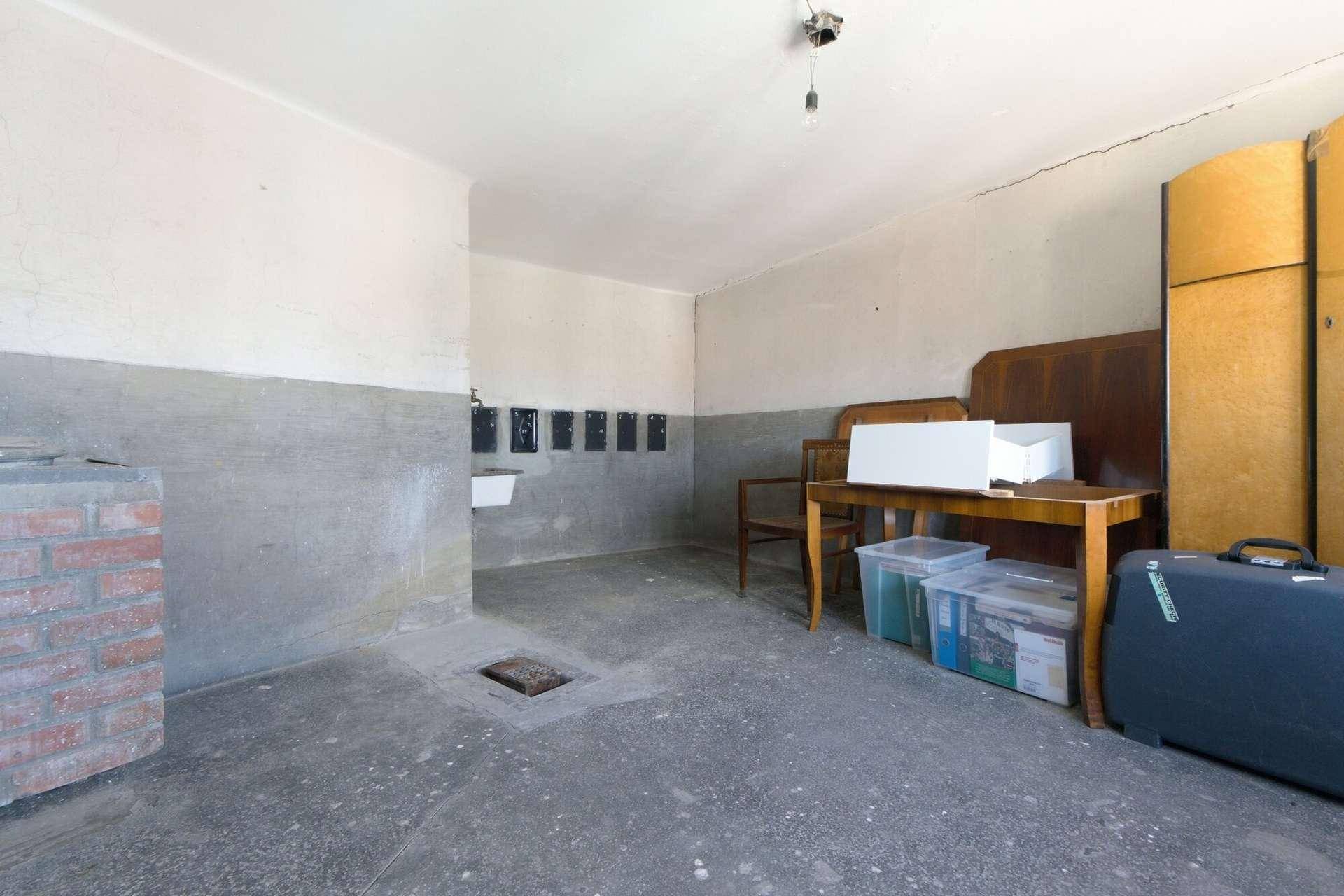 Unausgebauter Kellerraum mit Betonboden, Waschbecken und verschiedenen Gegenständen.