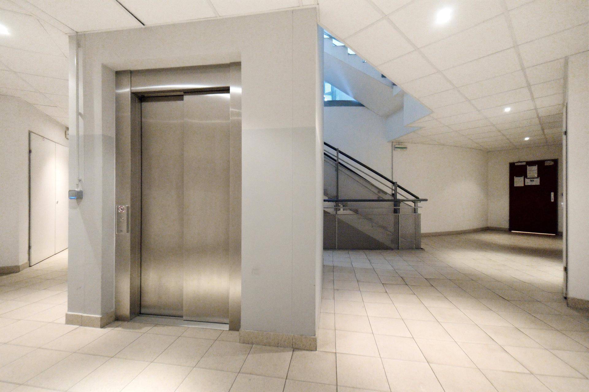 Moderner Flur mit Aufzug, Fliesenboden und Zugang zu den Wohnungen und dem Treppenhaus.