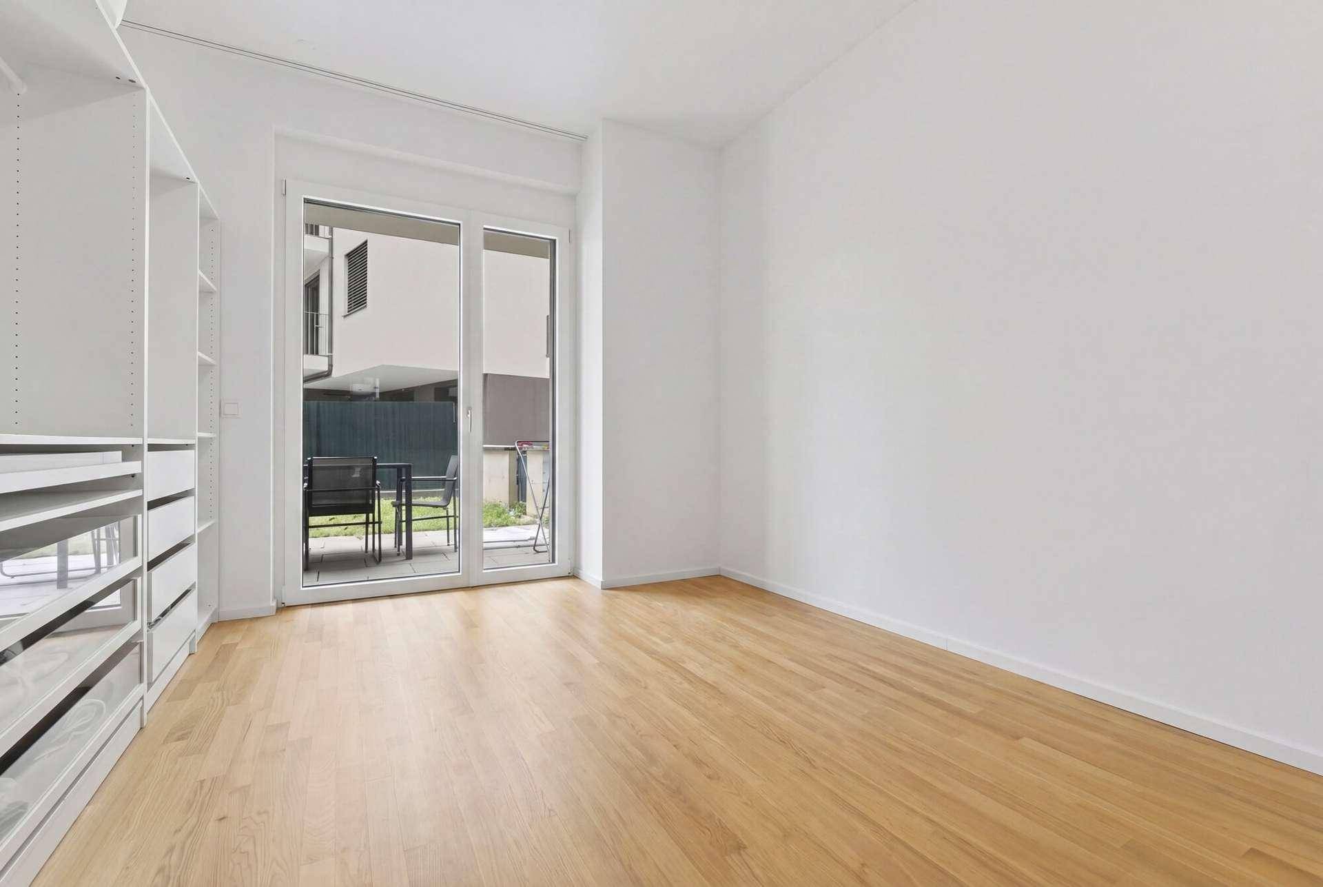 Helles Schlafzimmer mit Holzboden, Einbauschränken und Zugang zu einem möblierten Außenbereich.