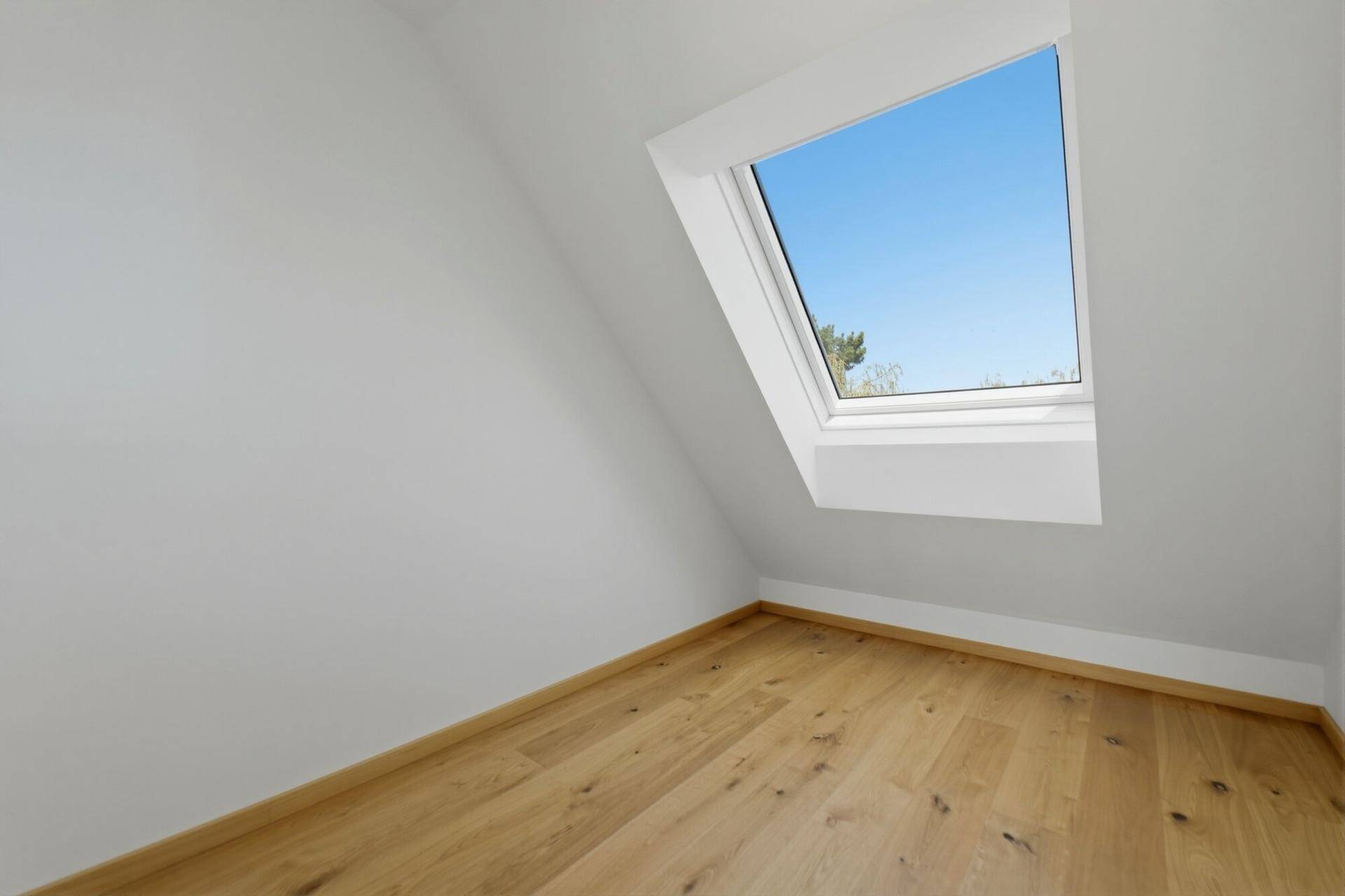 Helles Dachzimmer mit Holzboden und einem großen Dachfenster, das viel Licht spendet.