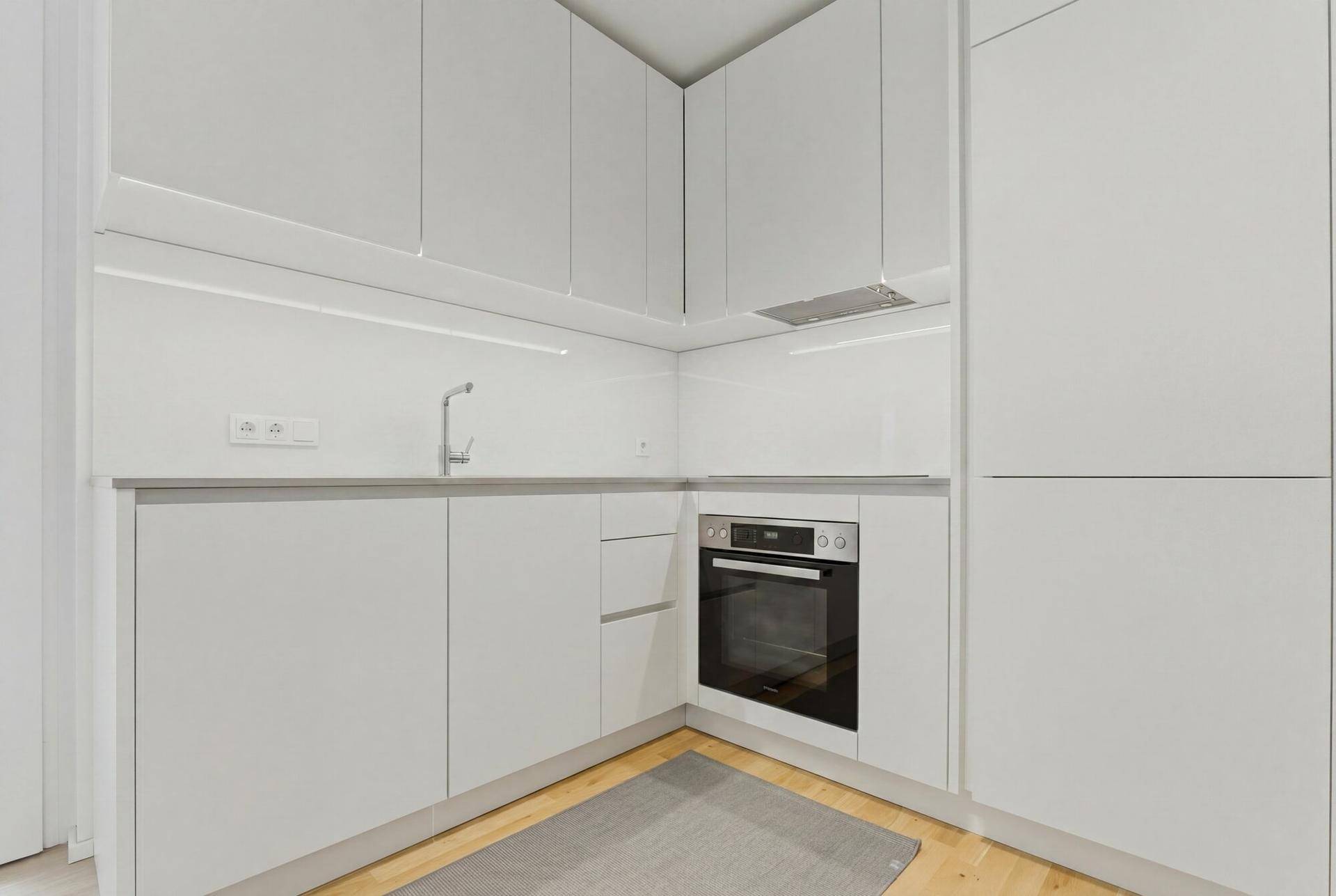 Moderne Einbauküche mit weißen Schränken, integriertem Backofen und heller Arbeitsplatte.