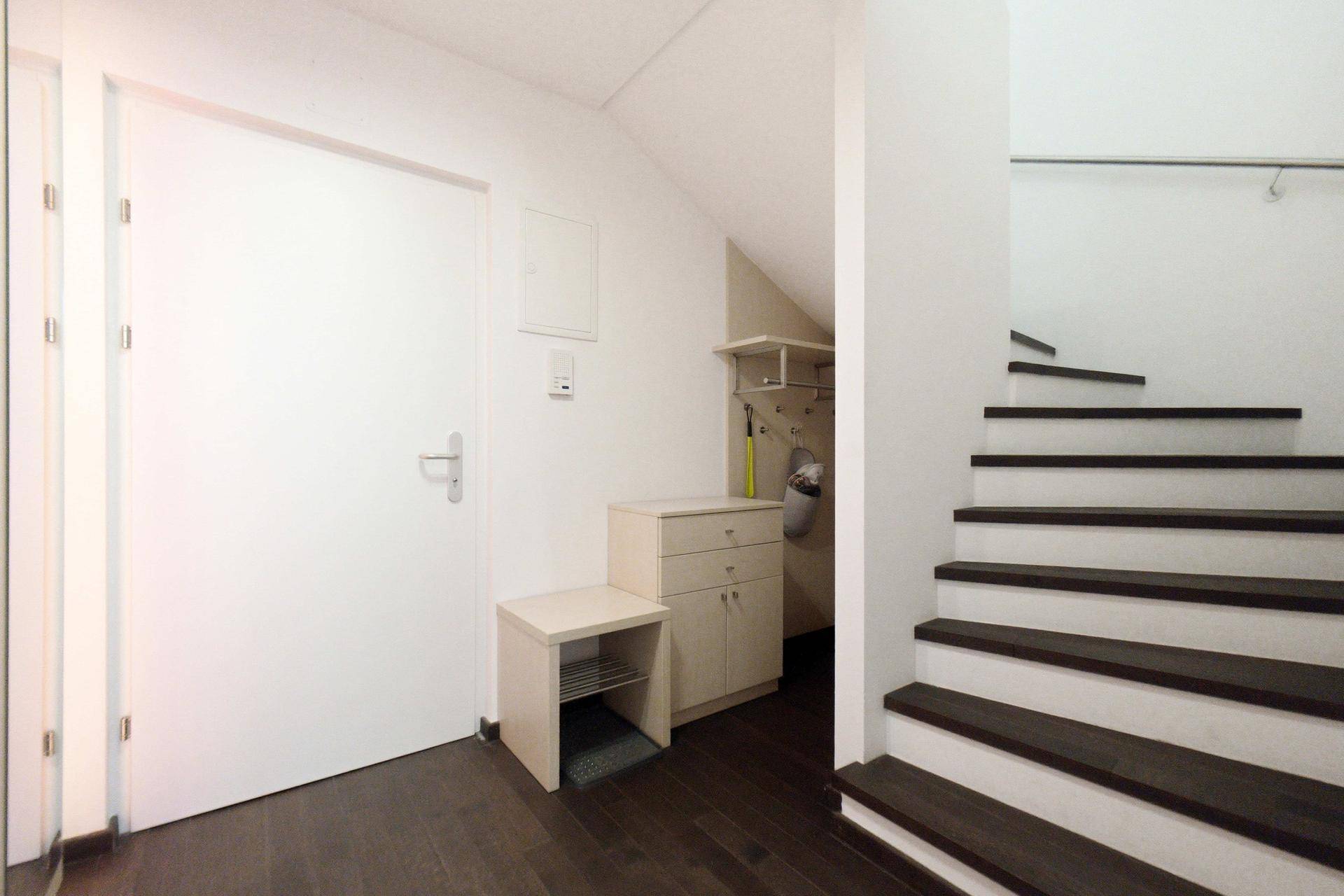 Heller Eingangsbereich mit dunklem Holzboden, praktischen Möbeln und Zugang zur Treppe.