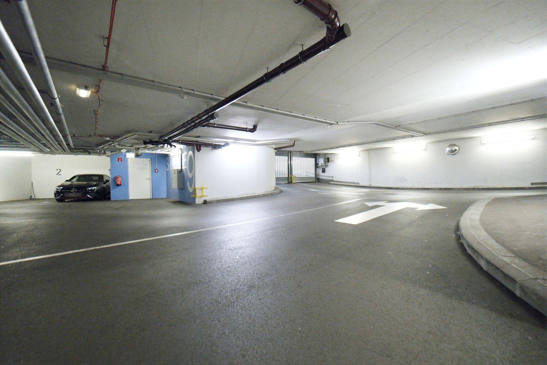 Helle Tiefgarage mit Fahrbahnmarkierungen, einer Kurve und einem geparkten Fahrzeug.