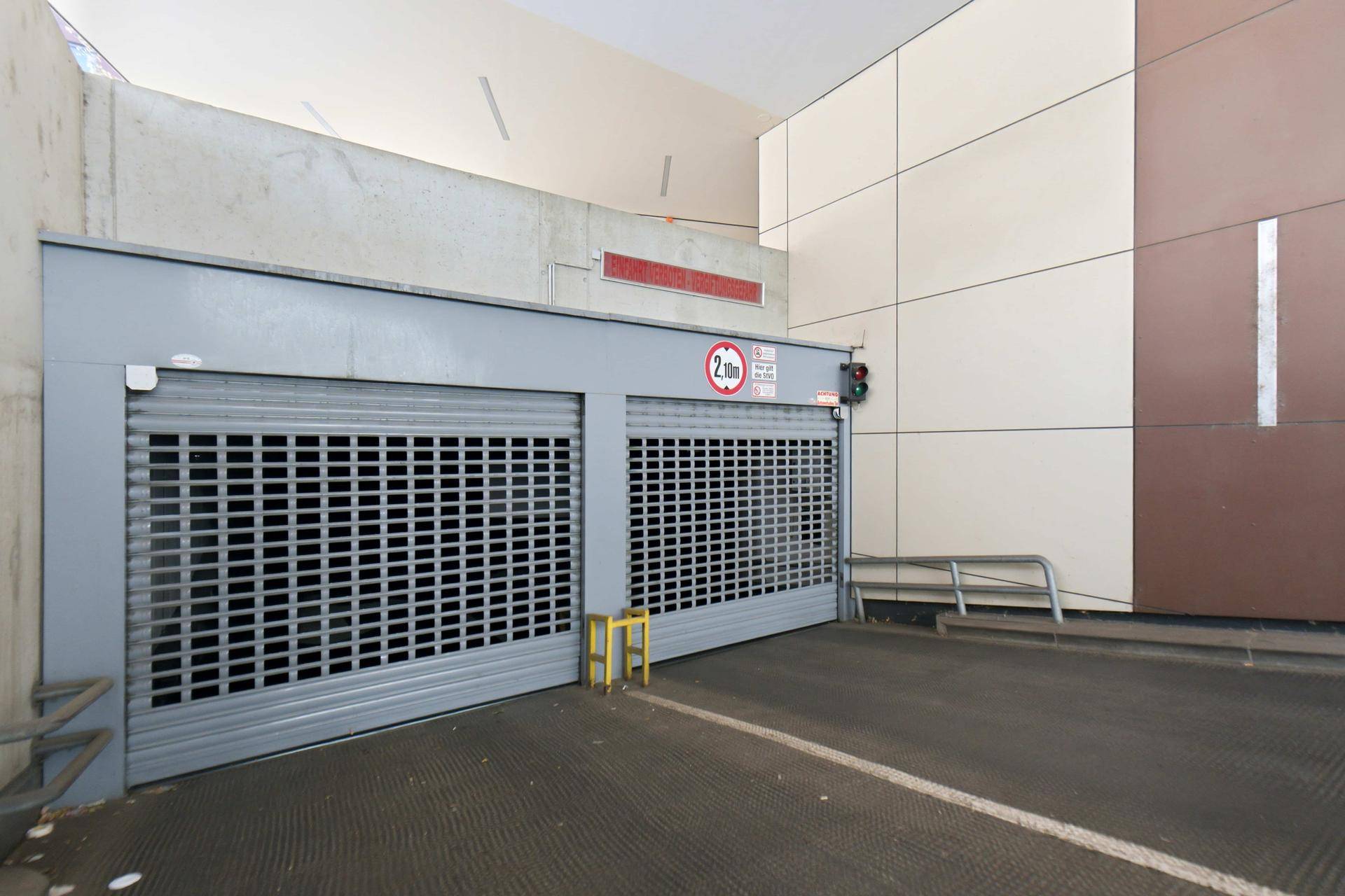 Geschlossene Rolltore der Tiefgarage mit Höhenbegrenzungsschild und moderner Fassade.
