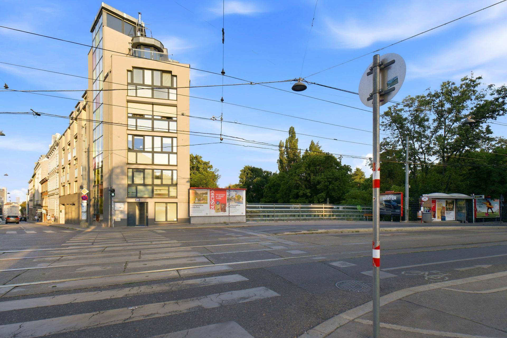 Modernes Gebäude an einer Straßenecke mit großen Fenstern und städtischer Umgebung.