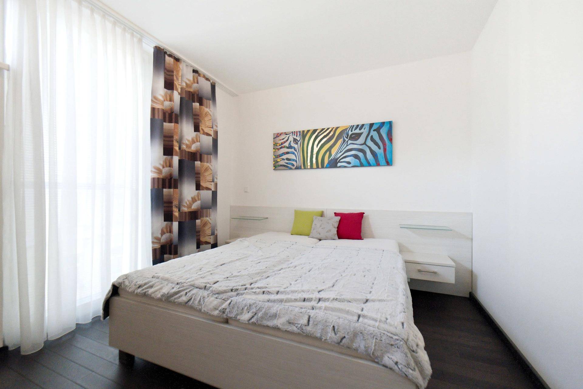 Schlafzimmer mit Doppelbett, farbenfrohem Kunstwerk und dunklem Holzboden, bietet eine moderne Einrichtung.