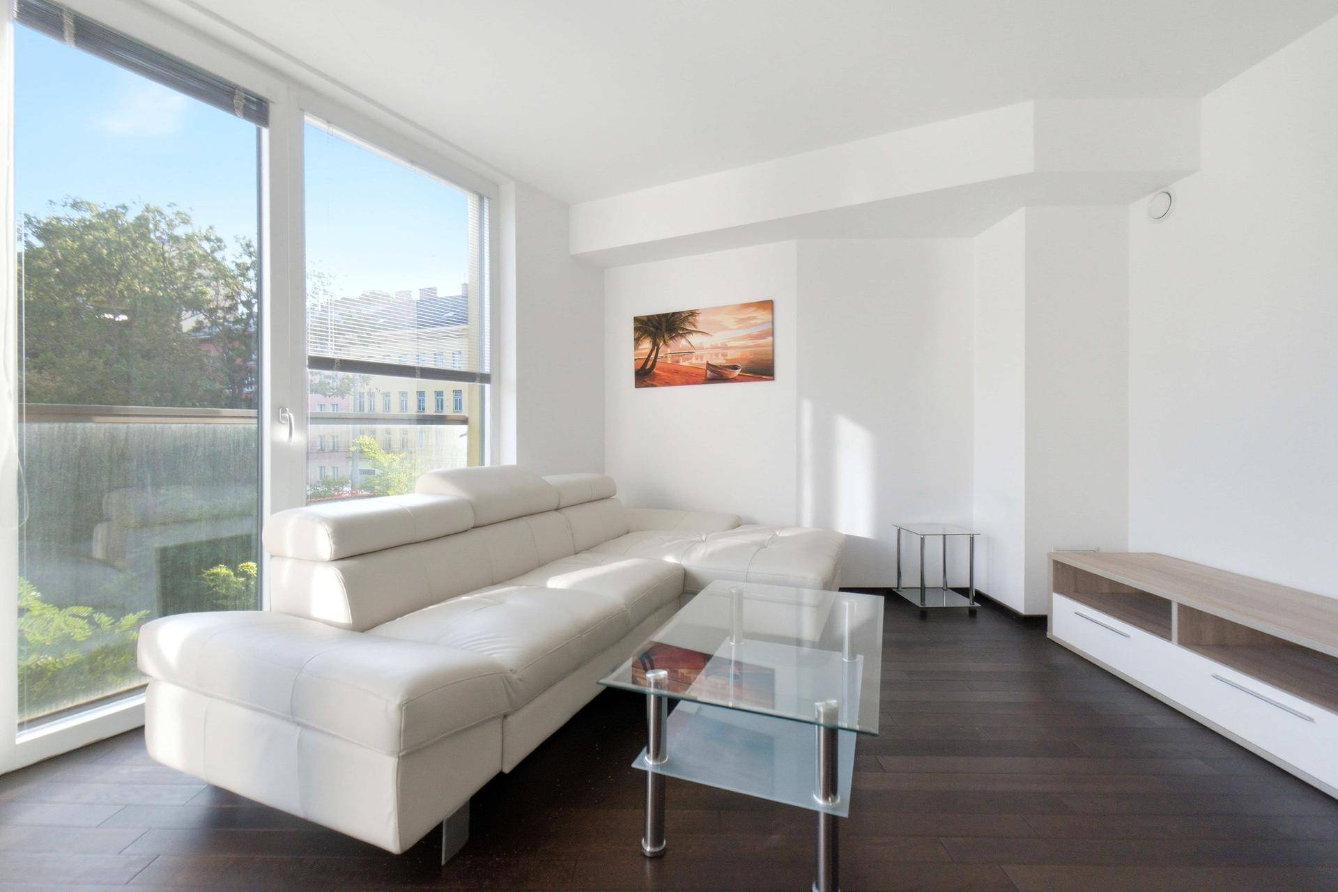 Lichtdurchflutetes Wohnzimmer mit beigem Ecksofa, Glascouchtisch und Blick auf die Stadt.