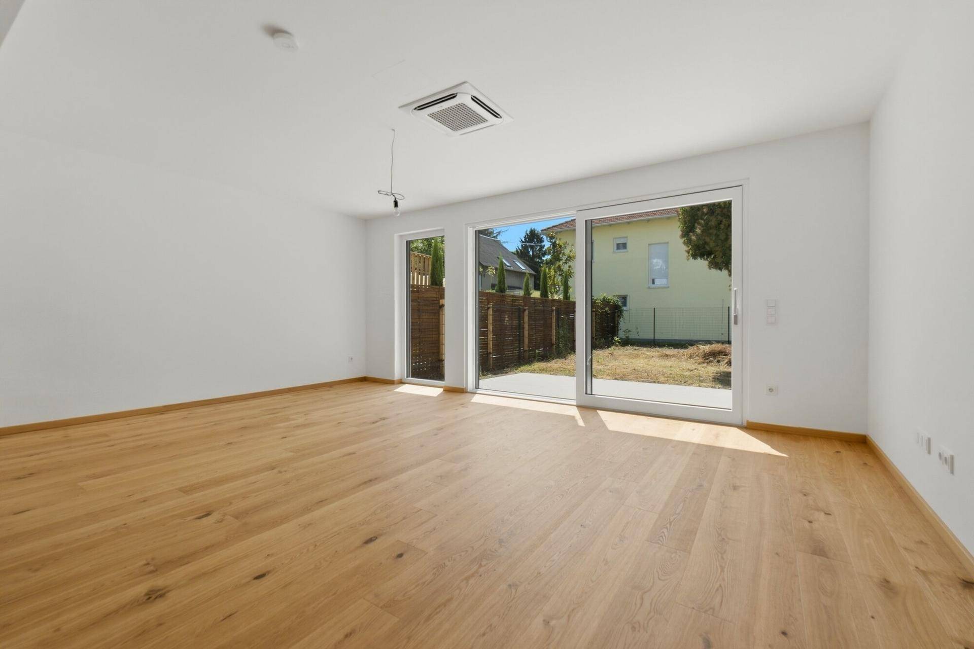 Geräumiges, unmöbliertes Wohnzimmer mit Holzboden und Schiebetüren zum Garten.