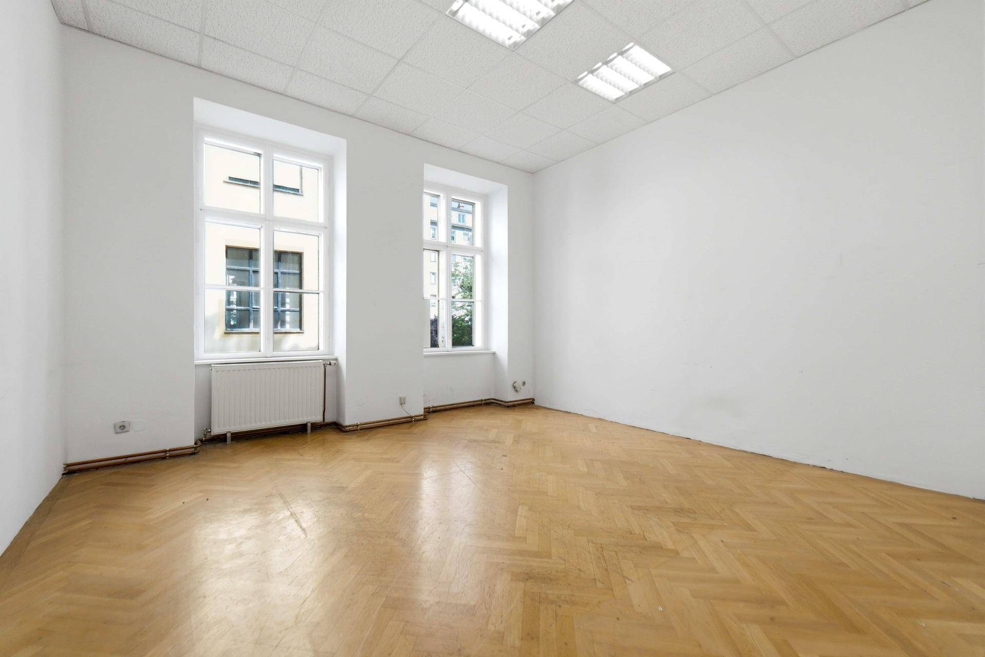 Heller Raum mit Fischgrätparkettboden und zwei großen Fenstern, ideal für Büro oder Wohnen.