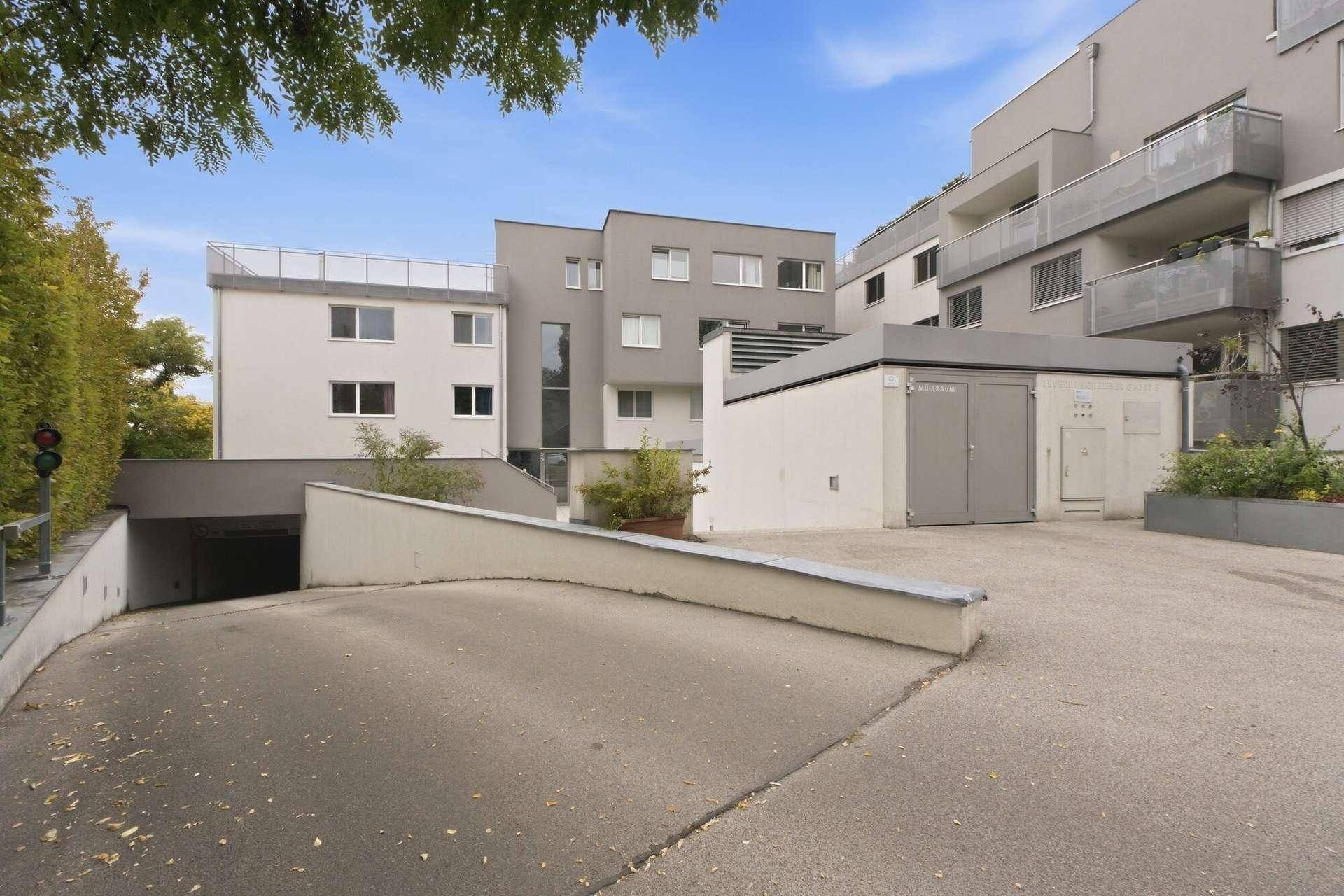 Modernes Mehrfamilienhaus mit Tiefgaragenzufahrt, Balkonen und Dachterrasse unter blauem Himmel.