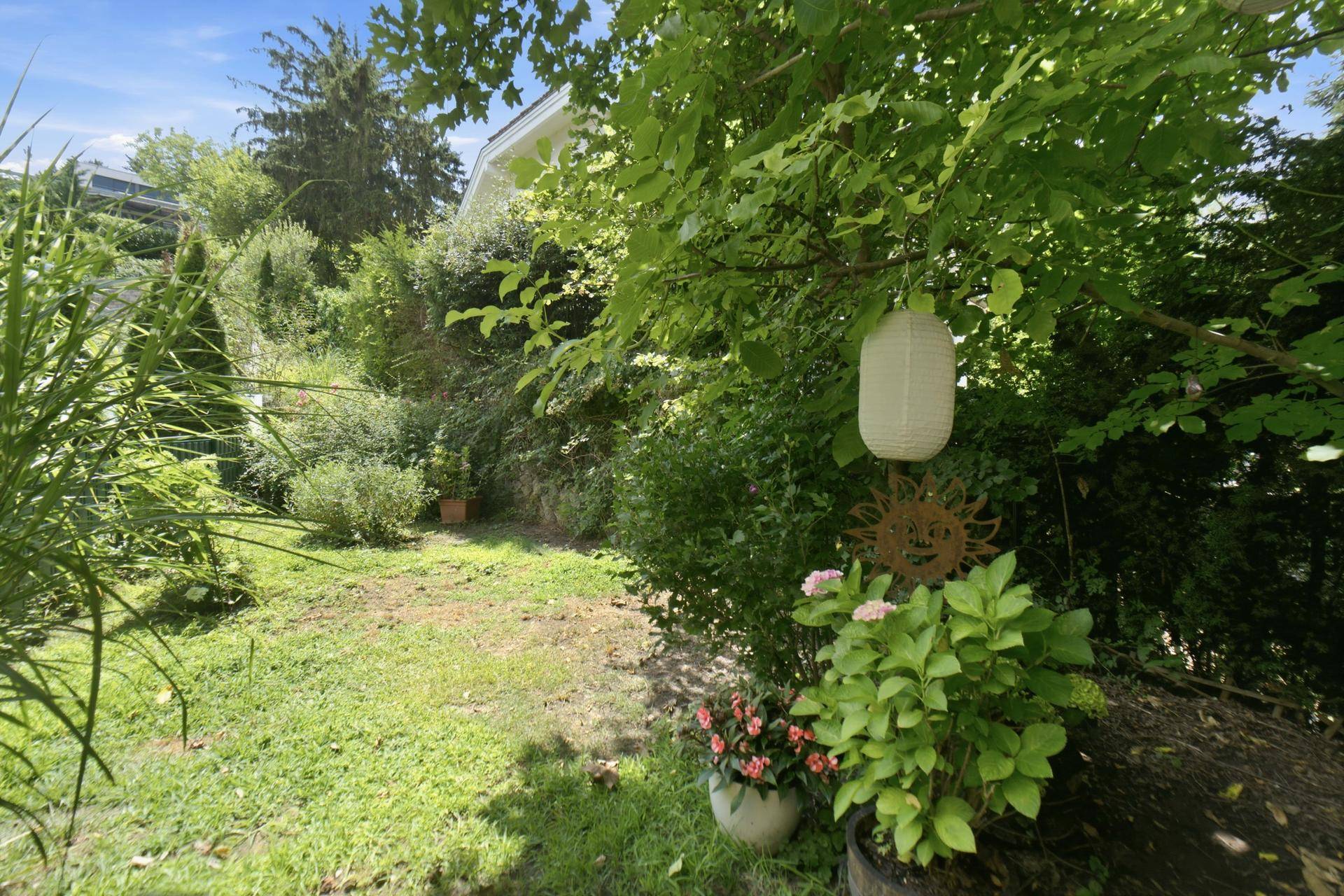 Gepflegter Gartenbereich mit Rasenfläche, Blumenbeeten und dekorativen Elementen.
