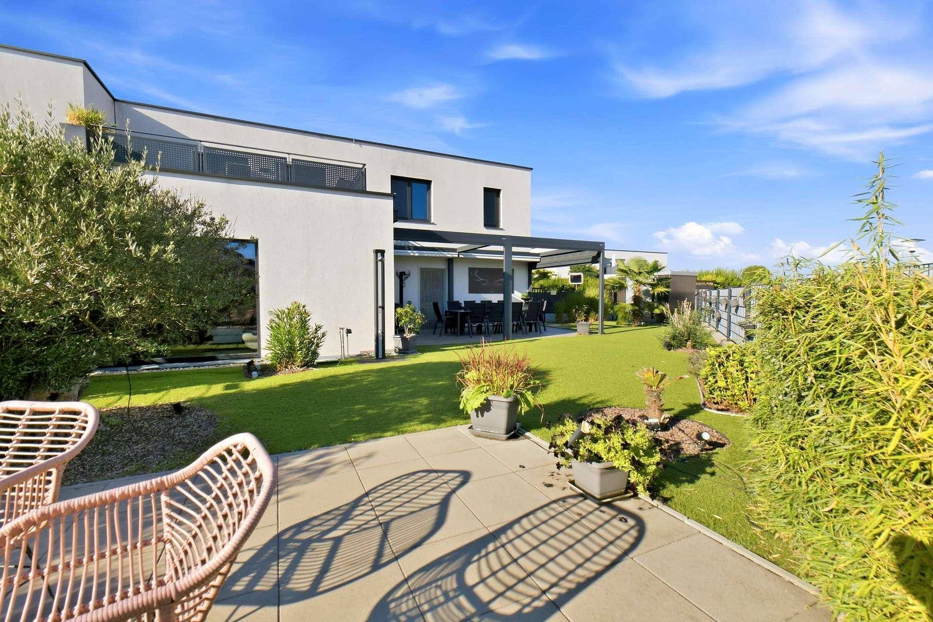 Weitläufiger Garten mit Rasenfläche und einer sonnigen Terrasse.